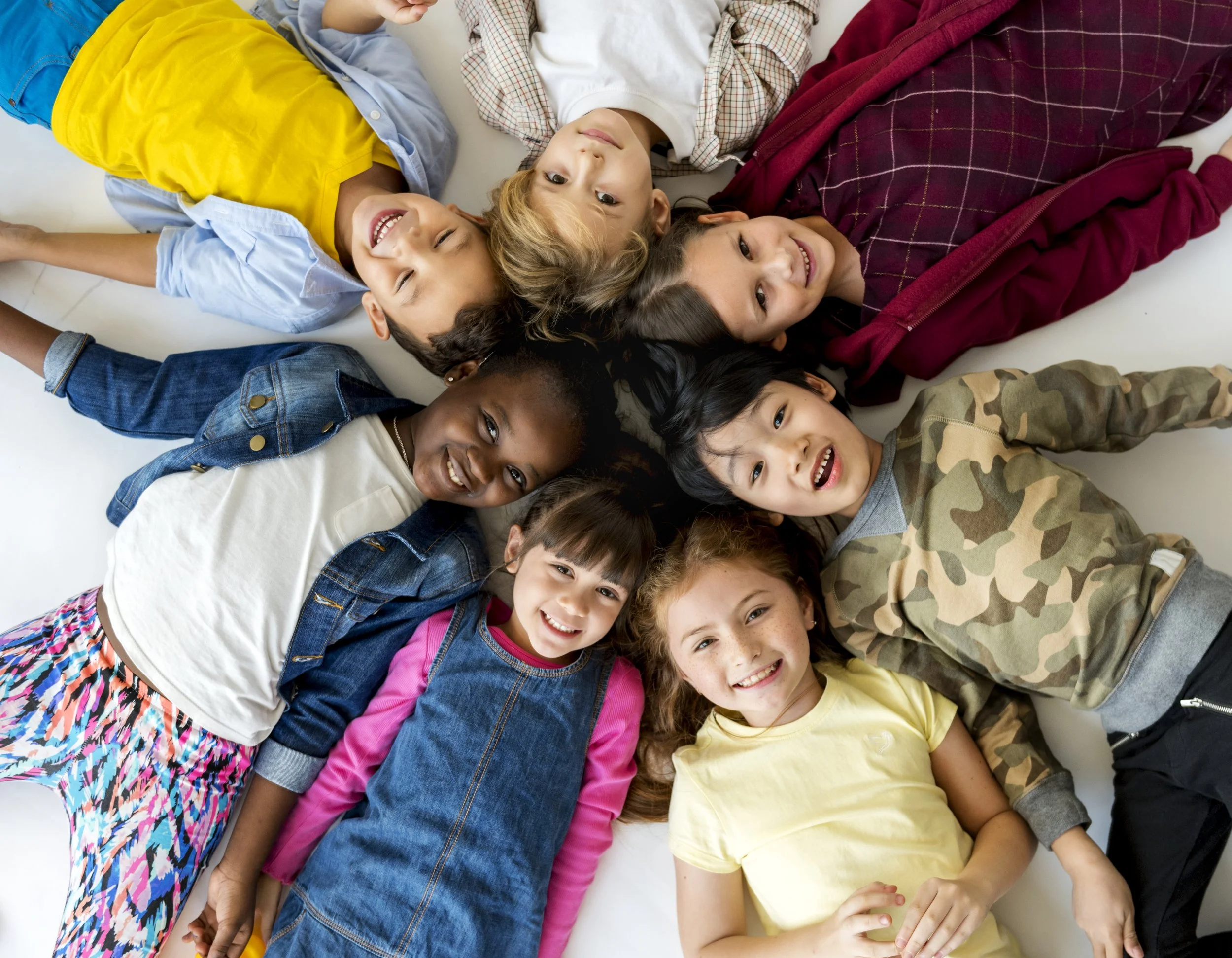 Diverse group of happy children lying together in a circle smiling, representing the inclusive and joyful pediatric occupational therapy services at Flourish Therapy Service in Athens, GA.