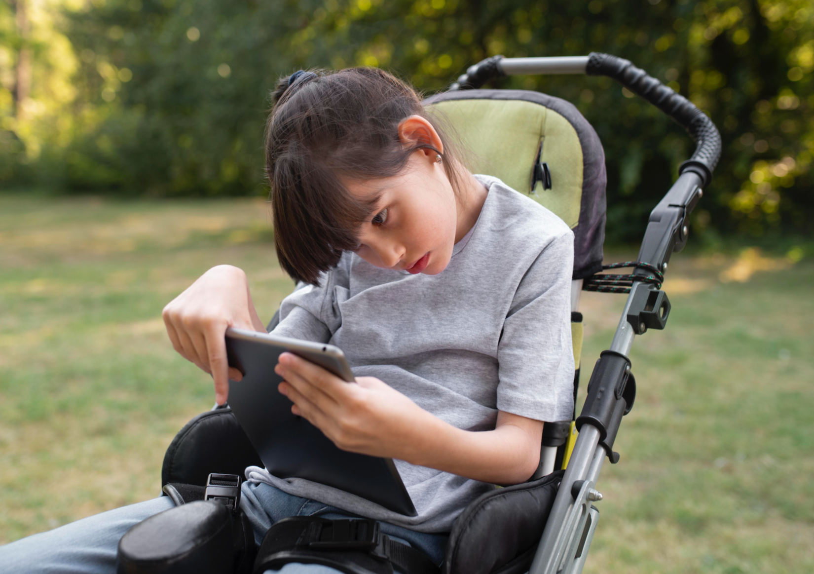 Child using a tablet device while seated in a wheelchair, representing assistive technology and adaptive equipment consultation services at Flourish Therapy Service in Athens, GA.