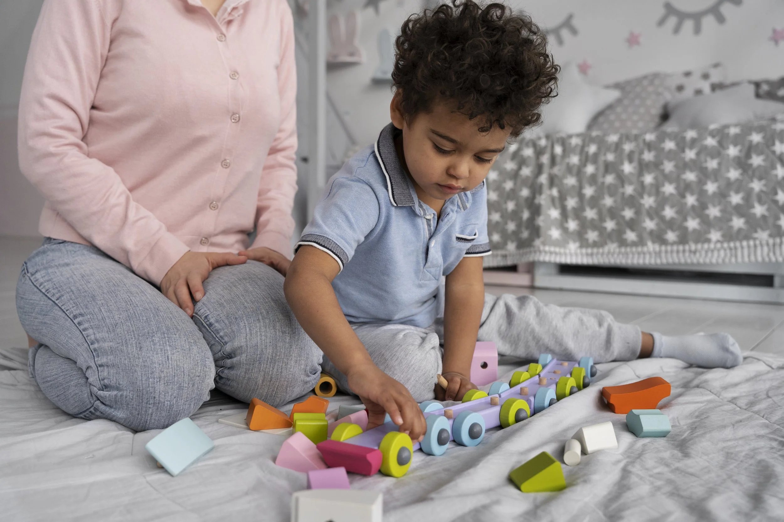 Therapist sitting on the floor with a young toddler playing with colorful toys, representing early childhood occupational therapy services at Flourish Therapy Service in Athens, GA.
