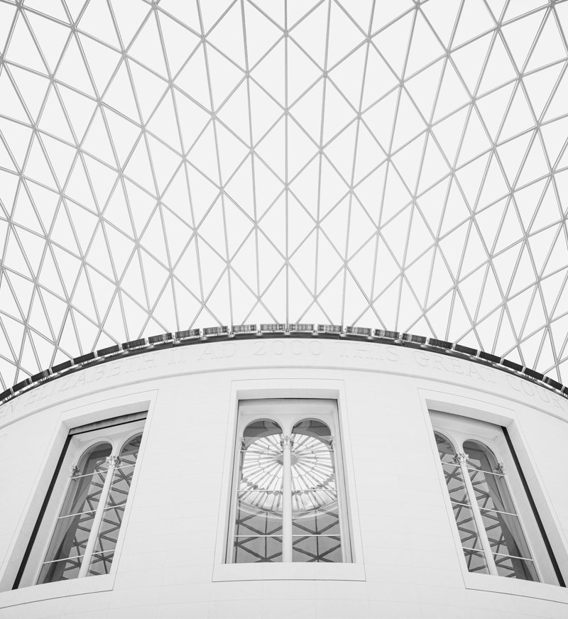 Interior view of a dome with a geometric lattice pattern and tall arched windows reflecting the sky.