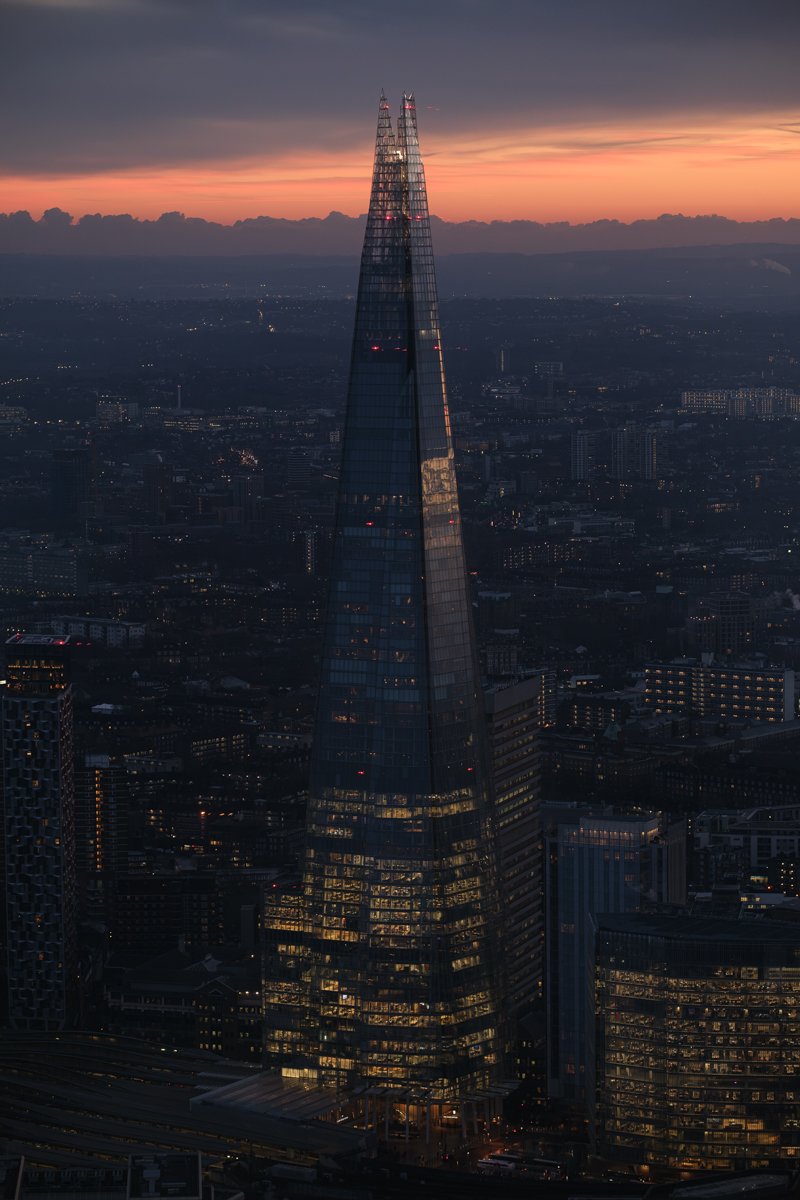 Skyline of London at sunset with The Shard skyscraper illuminated in the evening sky.