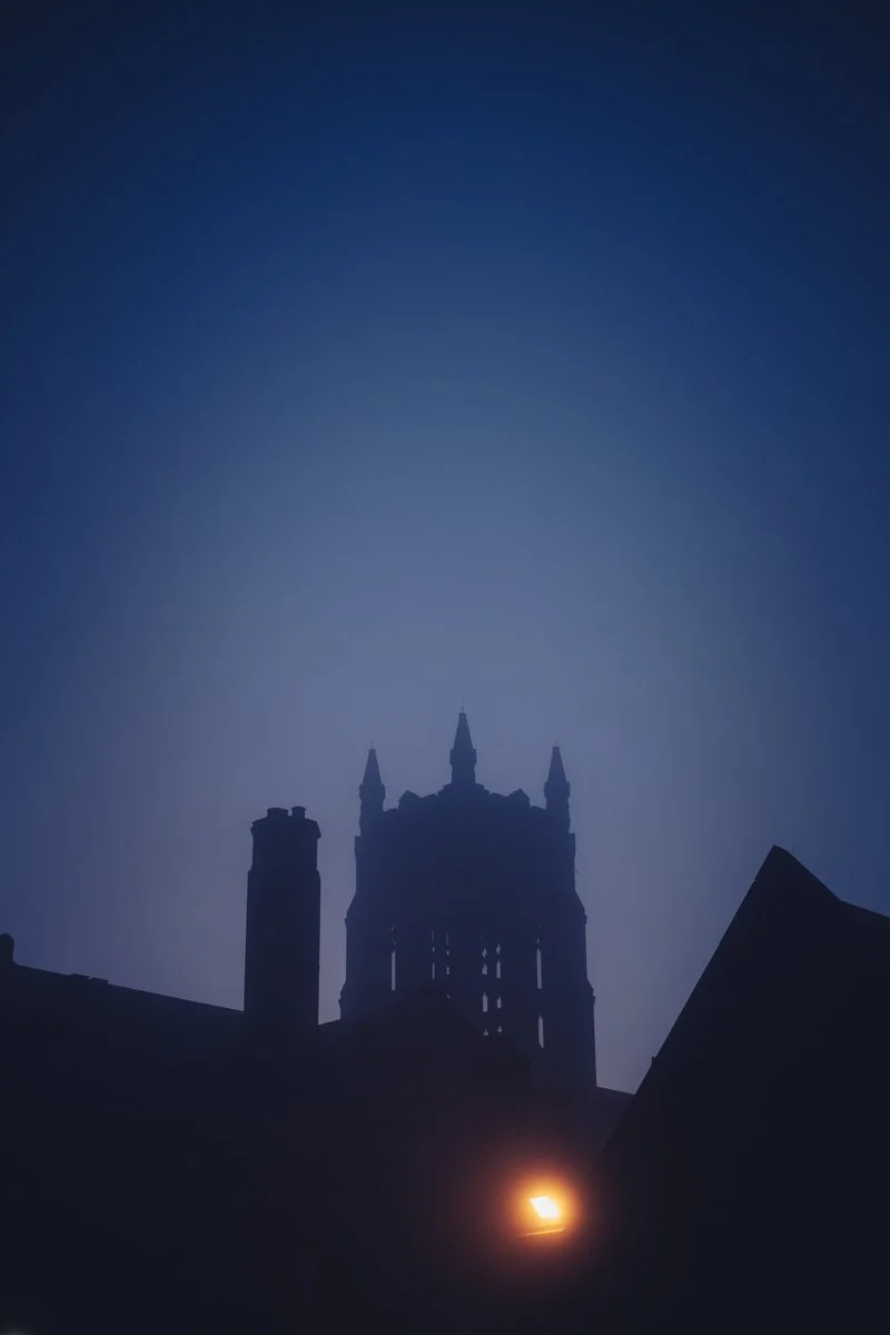 Night time photo of a gothic-style church silhouette with pointed towers, with a streetlamp glowing below.