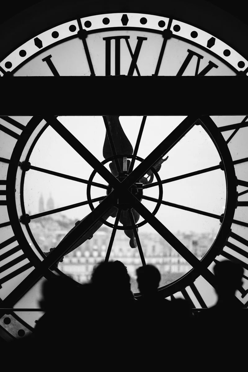 Black and white photo of a clock face viewed from inside, with the silhouette of three people in the foreground.