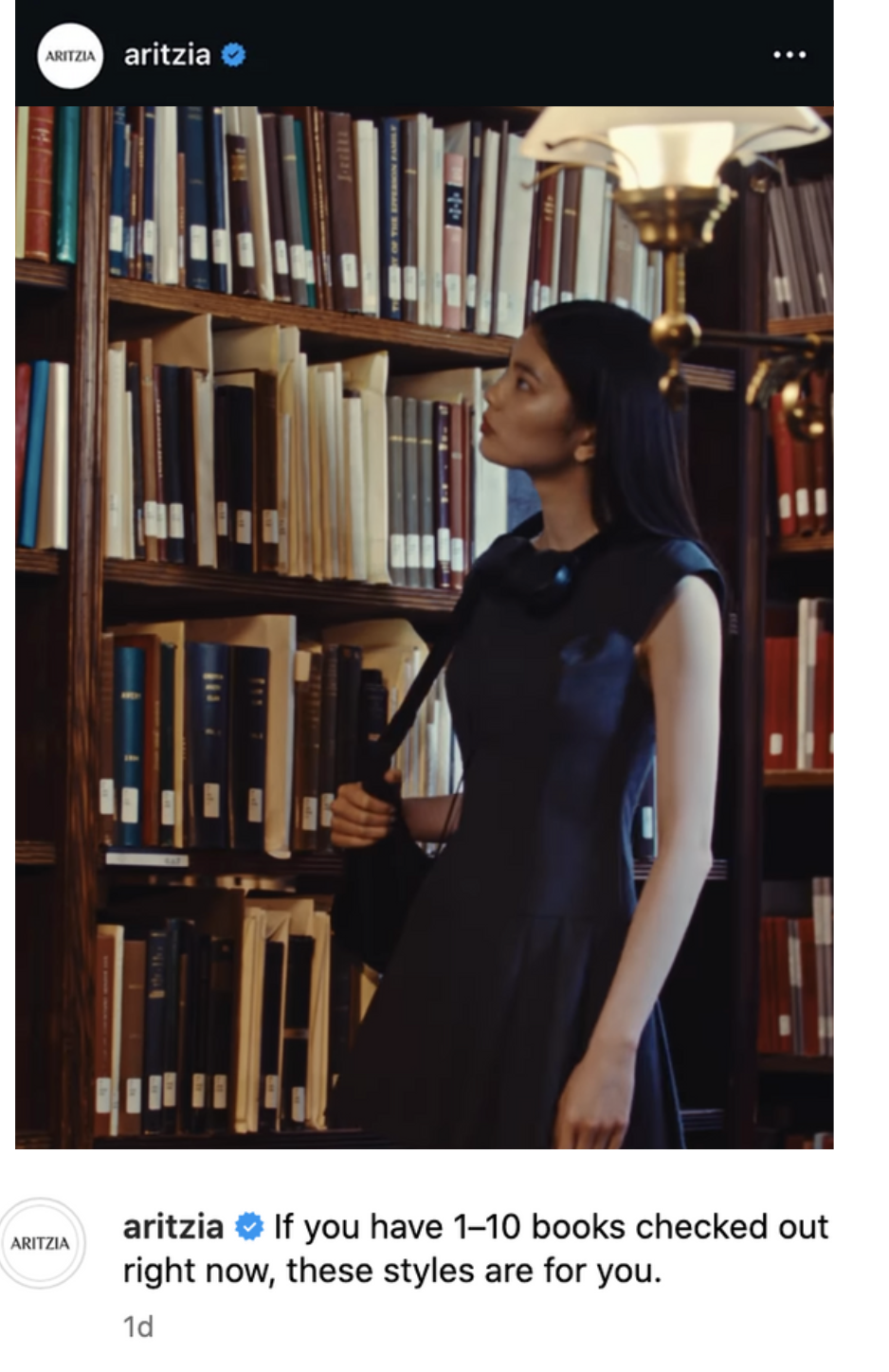 A woman in a black dress stands in a library aisle, looking at the books on the shelves.