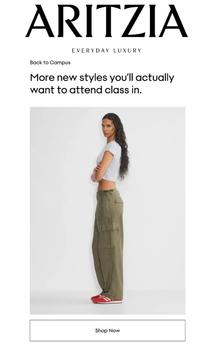 A woman standing sideways with her arms crossed, wearing a white crop top, green cargo pants, and red sneakers, against a plain white background, promoting fashion styles for back-to-campus attire.