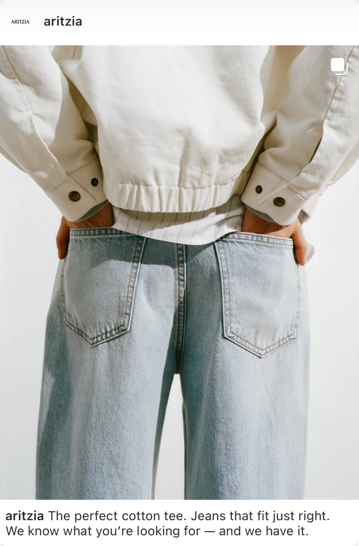 Back view of a person wearing light-wash jeans and a cream-colored jacket with hands in pockets.