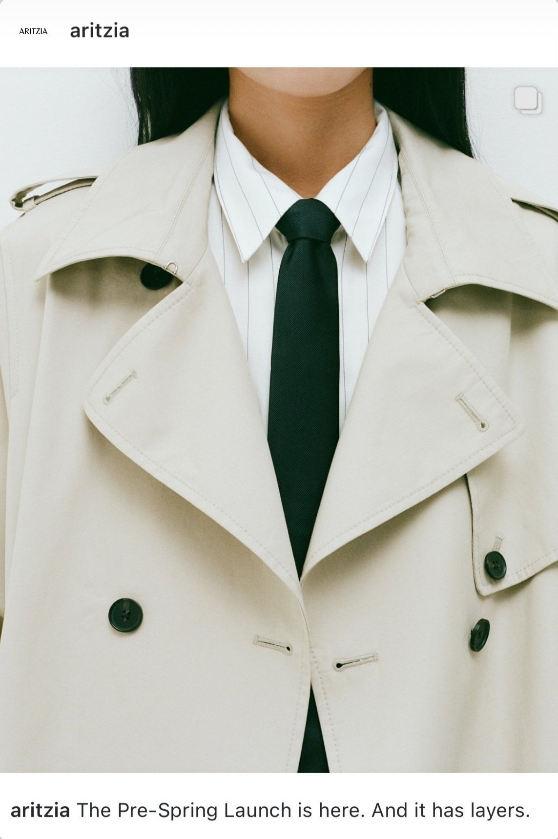 Close-up of a person wearing a beige trench coat, a white shirt with thin vertical stripes, and a black tie.