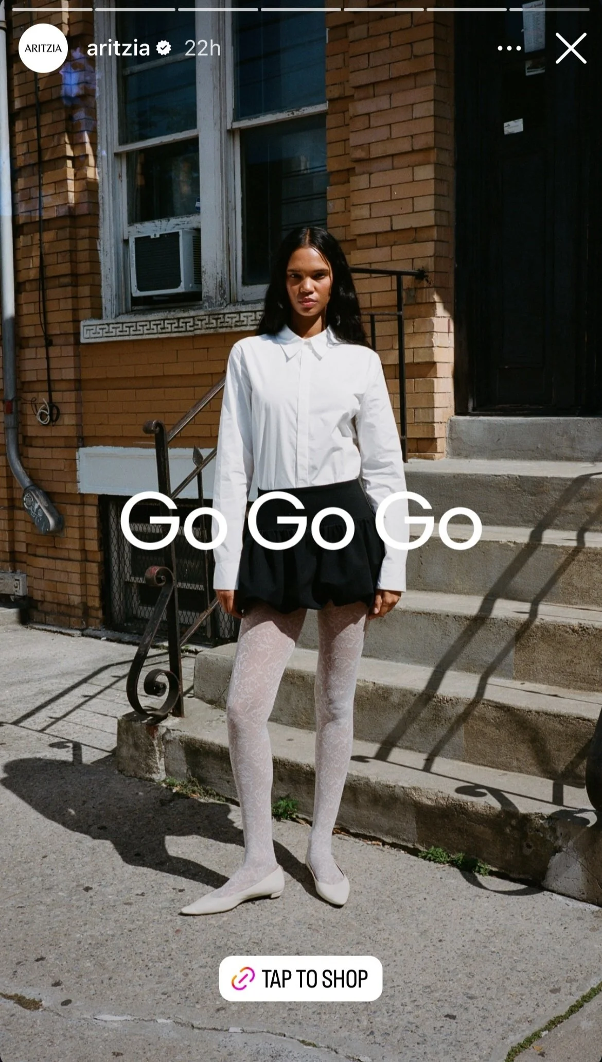 Woman standing outdoors on stairs wearing a white blouse, black skirt, white lace tights, and white shoes.