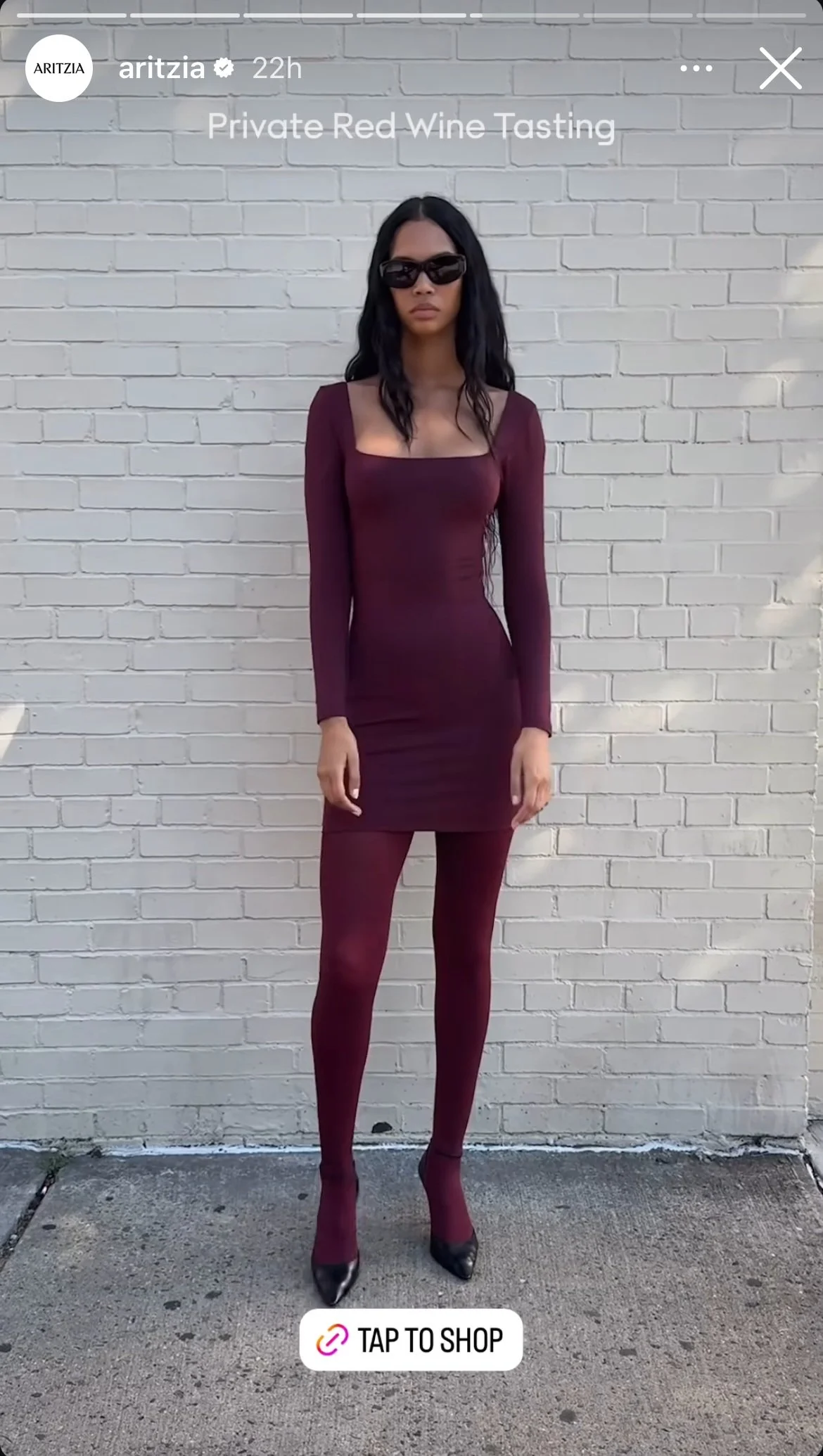 A woman with long dark hair wearing sunglasses, a burgundy long-sleeve dress, matching tights, and black heels standing in front of a white brick wall. The image promotes a private red wine tasting event.
