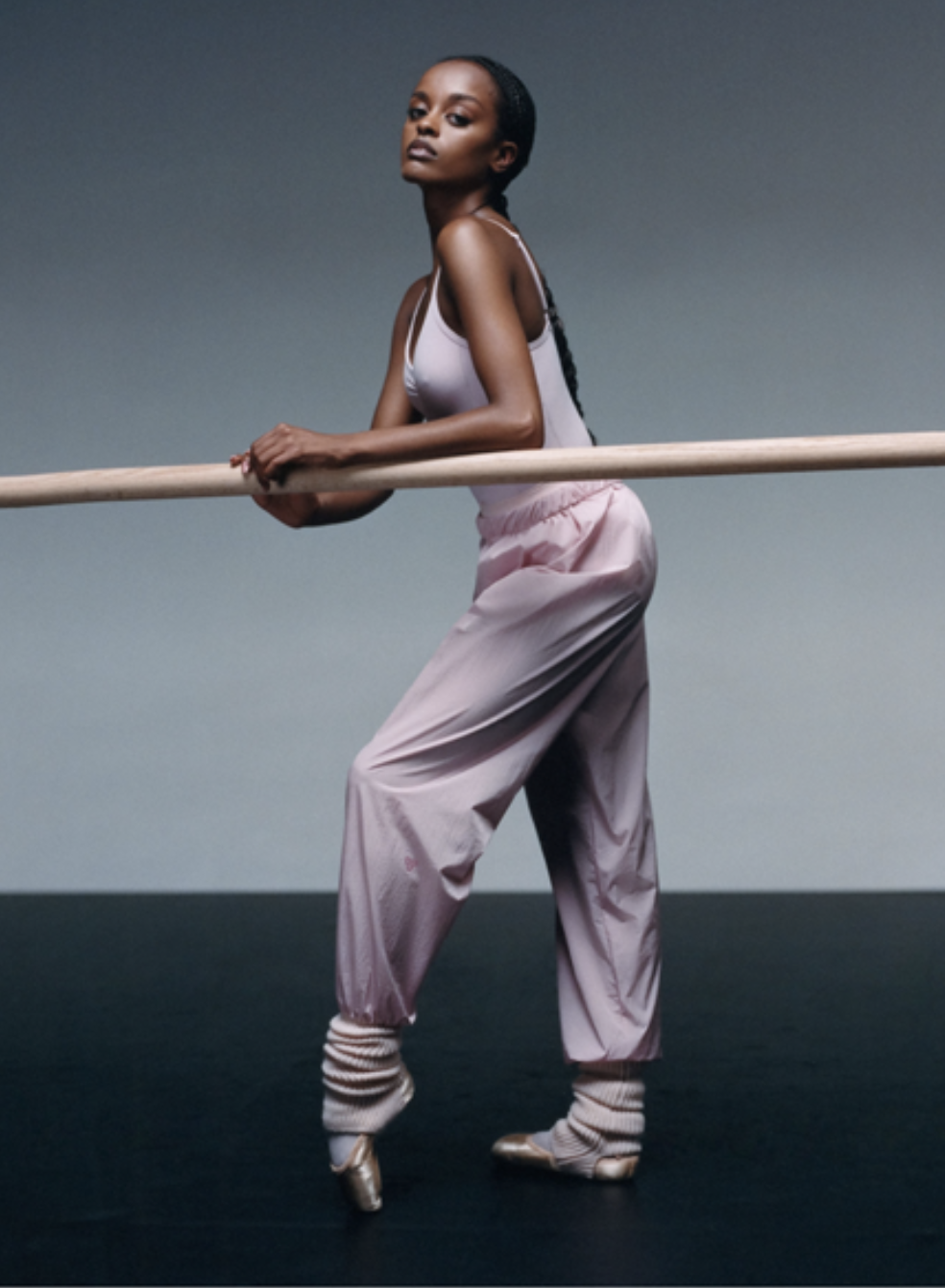 A graceful ballerina in pastel pink dance attire posed with a ballet barre, standing on pointe in a dance studio.