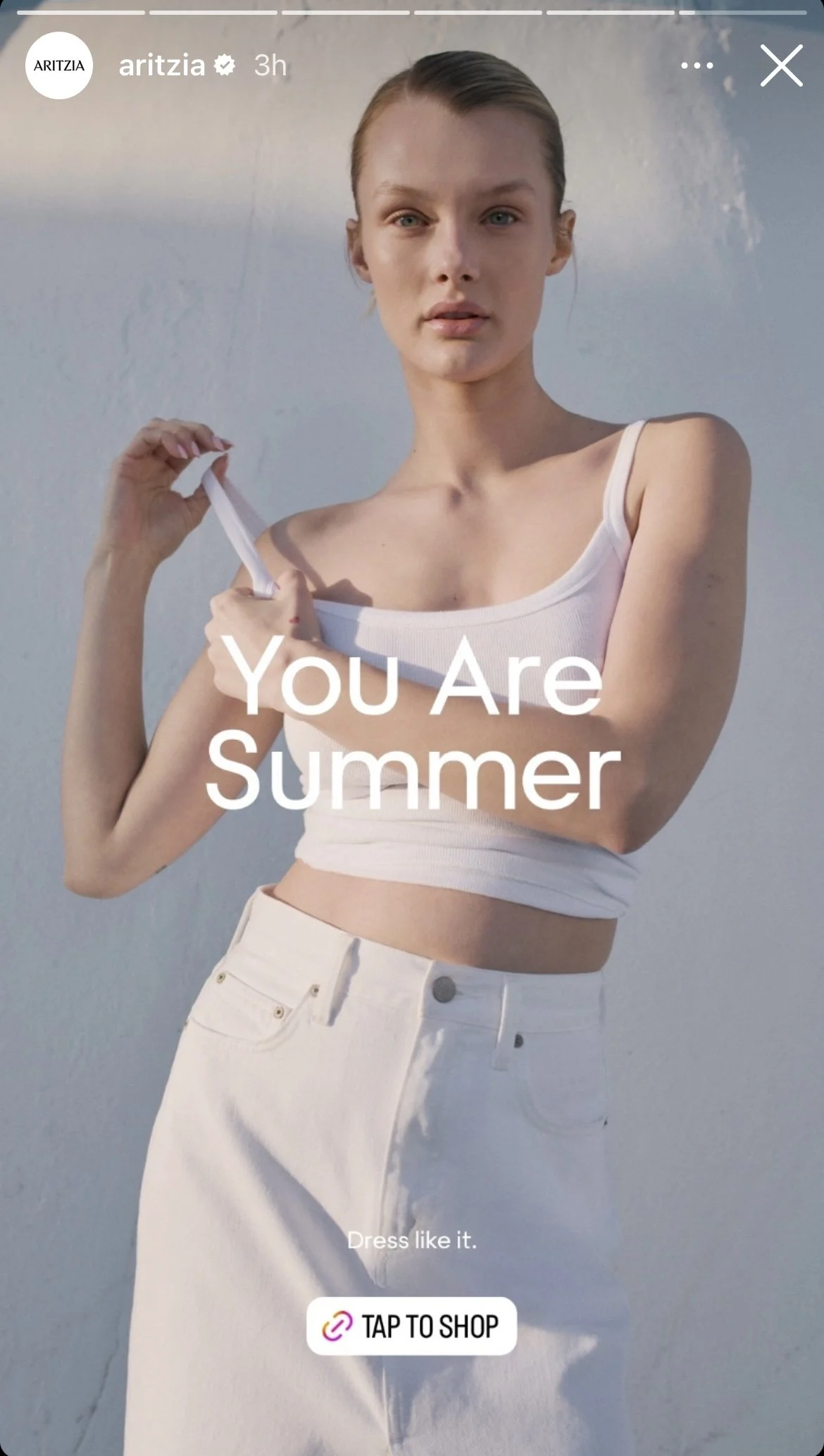 Young woman wearing a white tank top and white high-waisted pants, holding the strap of her top, with text "You Are Summer" and "Dress like it" over her. There is a prompt to tap to shop.