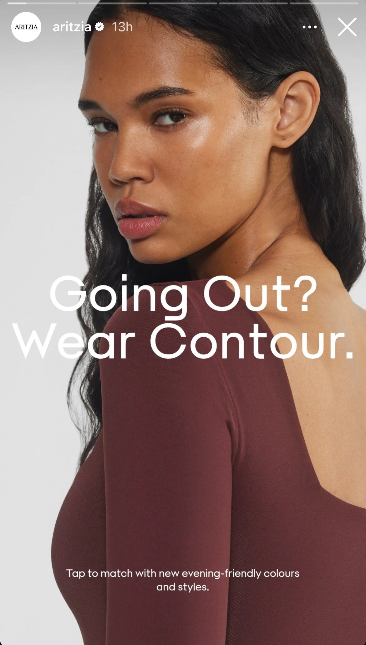 A woman with dark hair and a natural makeup look wearing a burgundy top, looking over her shoulder with text overlay that reads, "Going Out? Wear Contour. Tap to match with new evening-friendly colours and styles."
