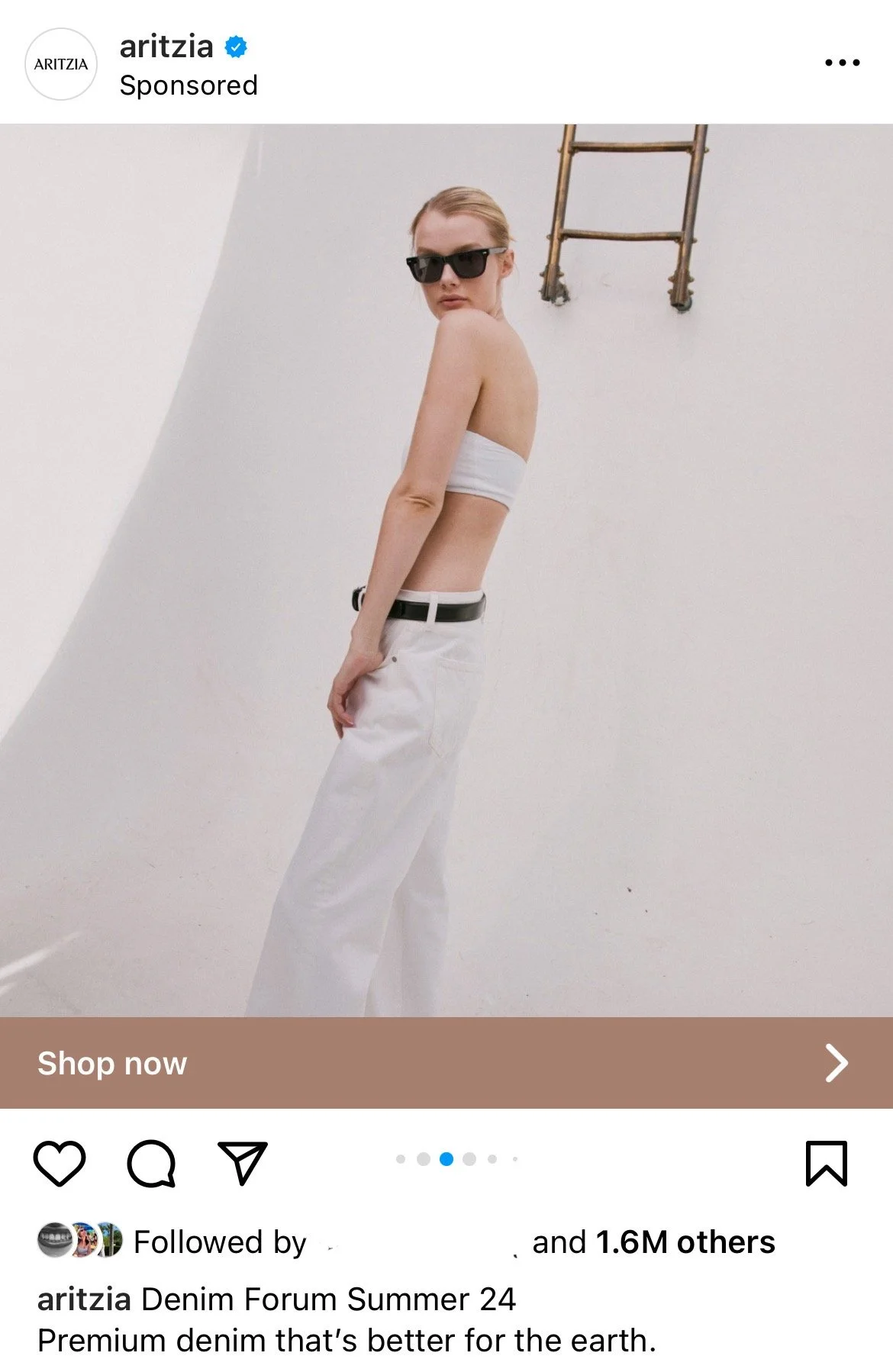 A woman in sunglasses and minimal clothing standing against a plain white wall with an old wooden ladder hanging on it, promoting denim apparel.