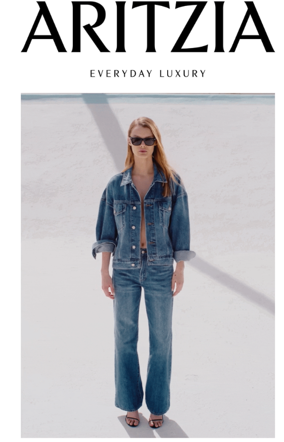 A woman standing on white sand or snow wearing a denim jacket and jeans, sunglasses, with text at the top that says 'ARITZIA' and 'Everyday Luxury' underneath.