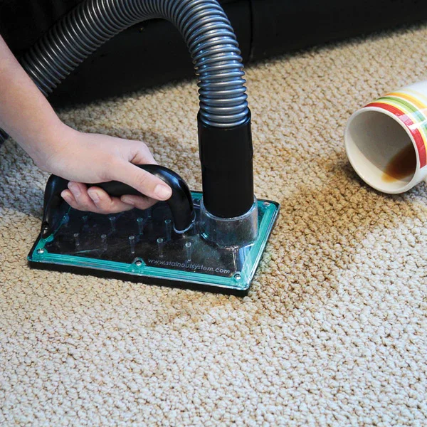 Person vacuuming carpet with a black hose attached to a central cleaning system, a coffee mug on its side nearby.
