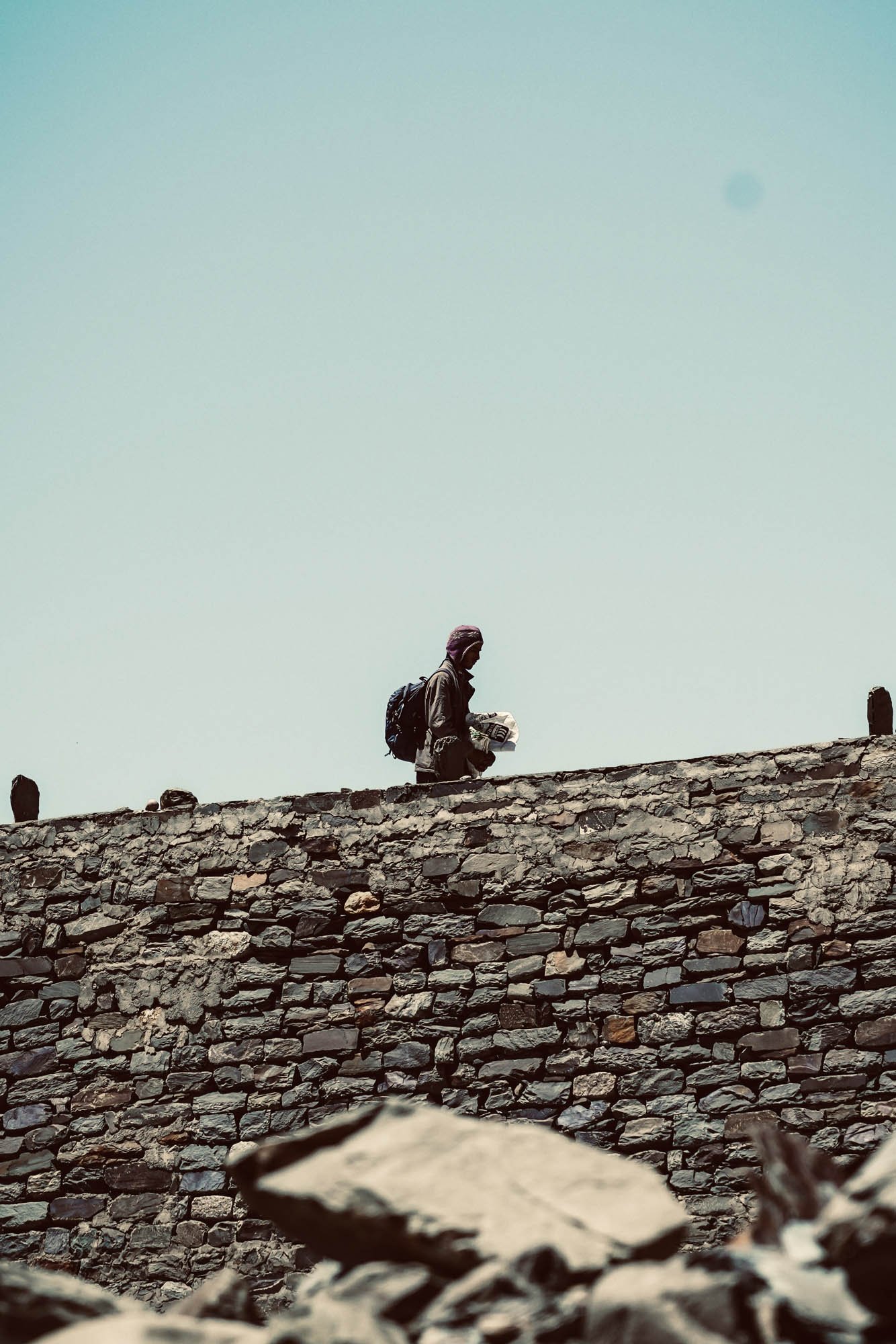 A person with a backpack walking on a rocky stone path under a clear sky.