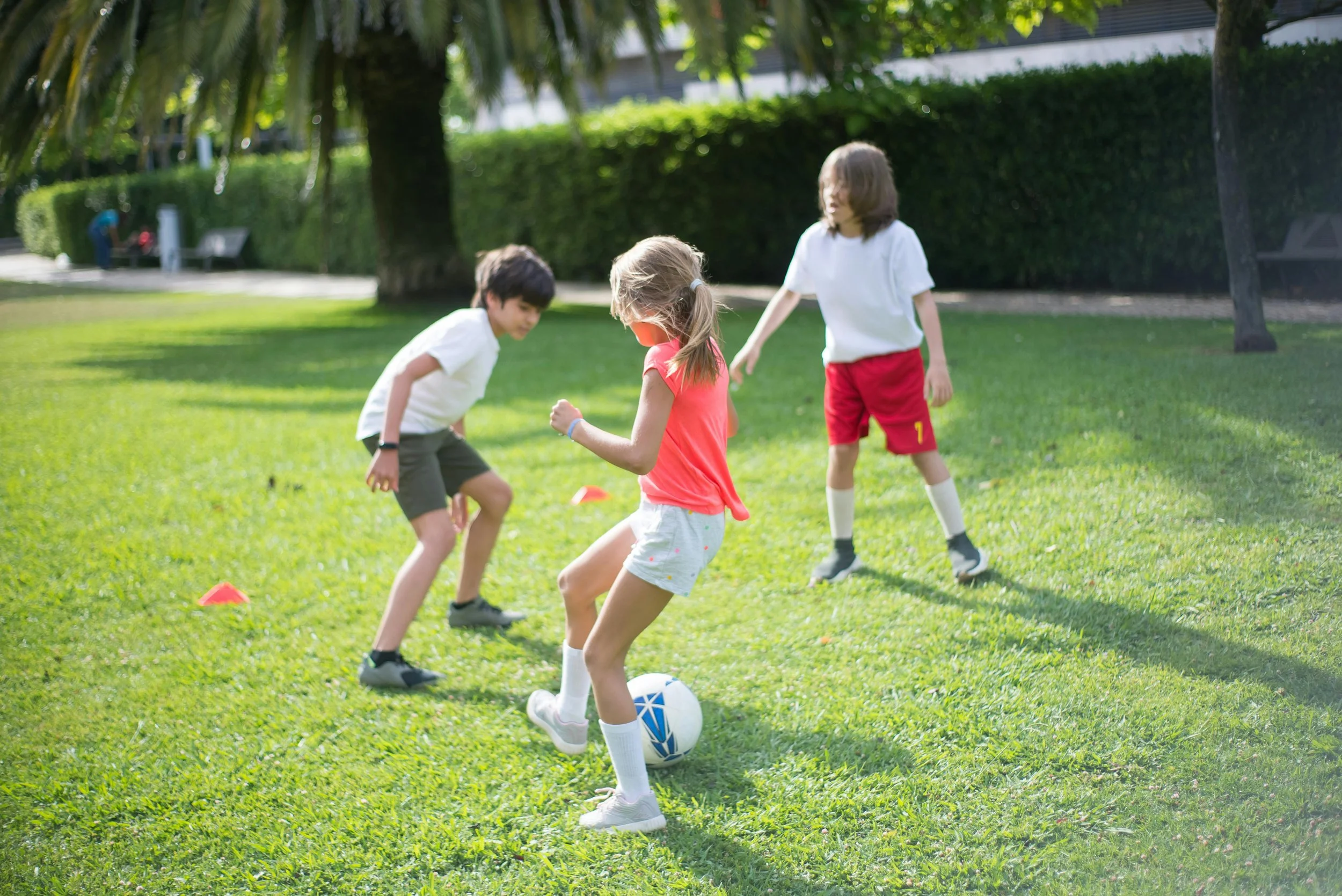 Three children playing soccer on a grassy field in a park.