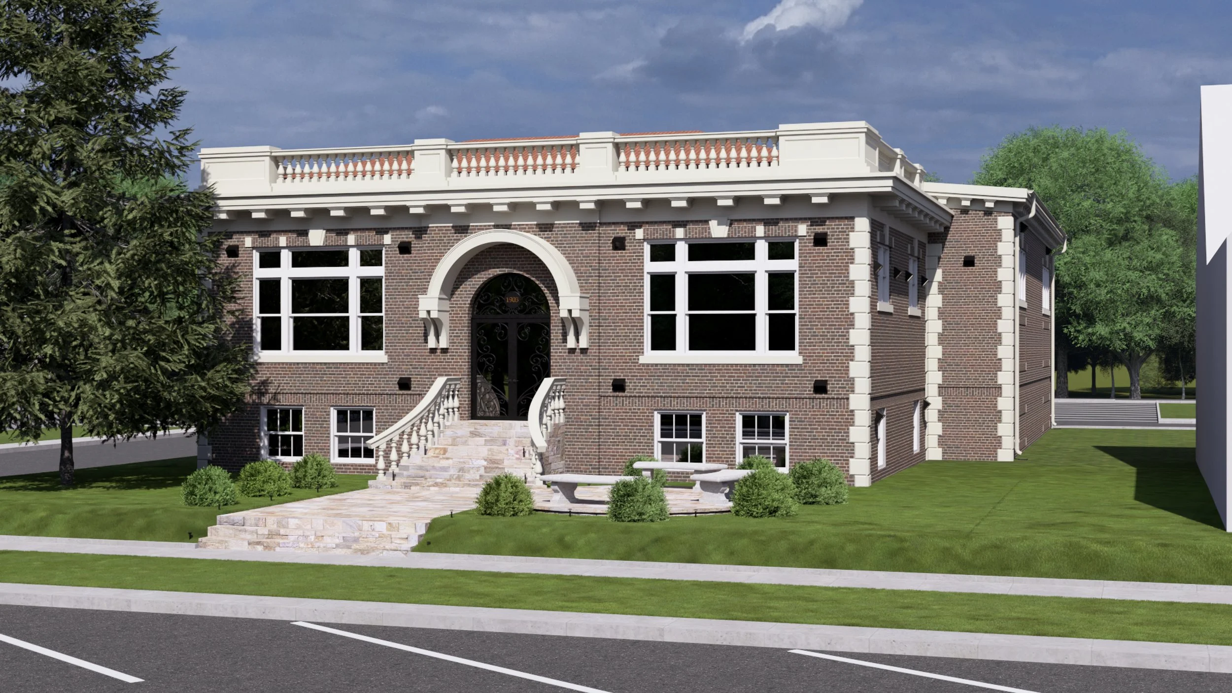 A two-story brick building with large windows, a decorative staircase leading to a main door, surrounded by a green lawn and trees, under a partly cloudy sky.