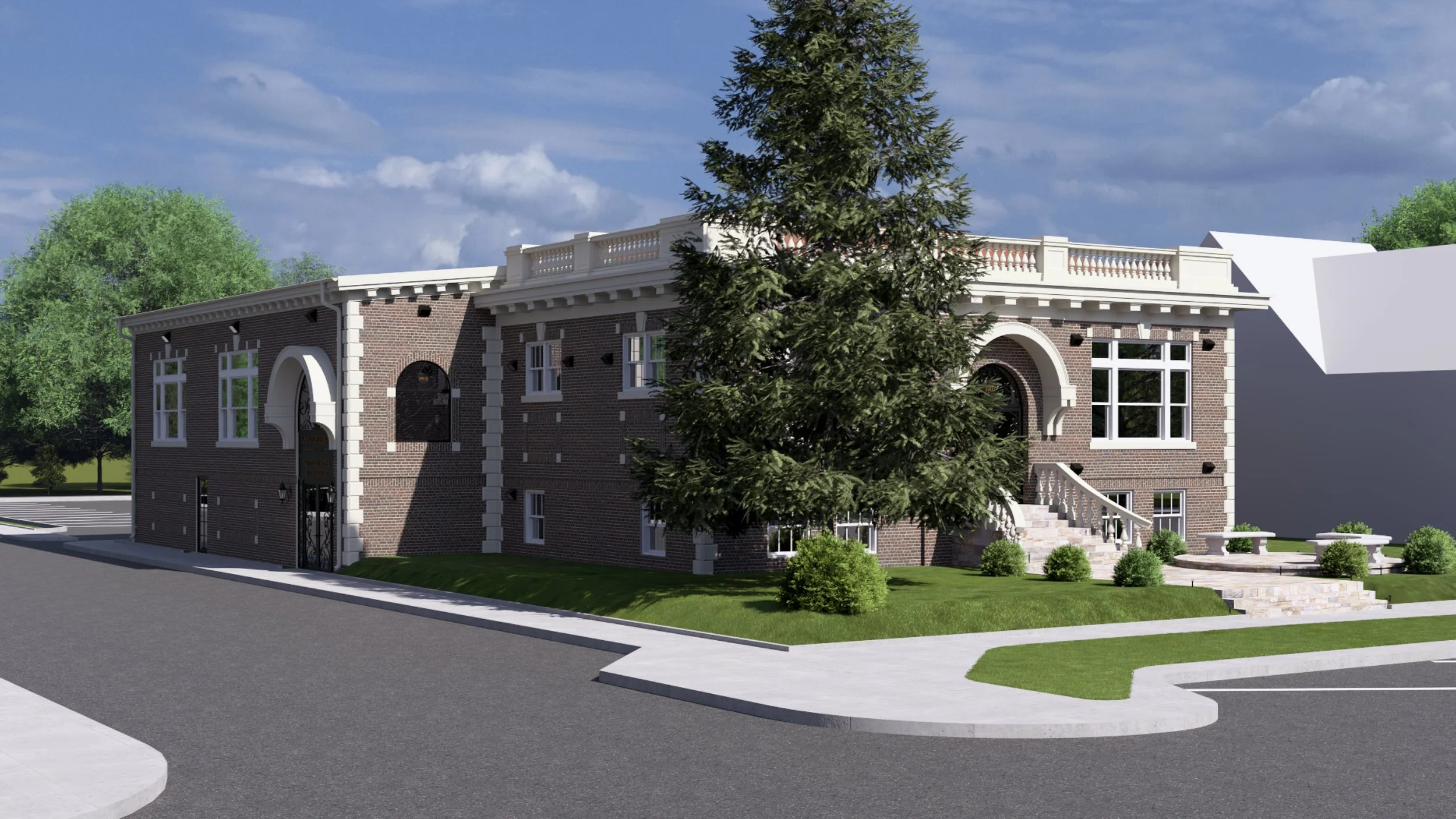 A two-story brick building with white architectural accents, large windows, and stairs leading to the entrance, surrounded by green trees and a landscaped lawn under a partly cloudy sky.