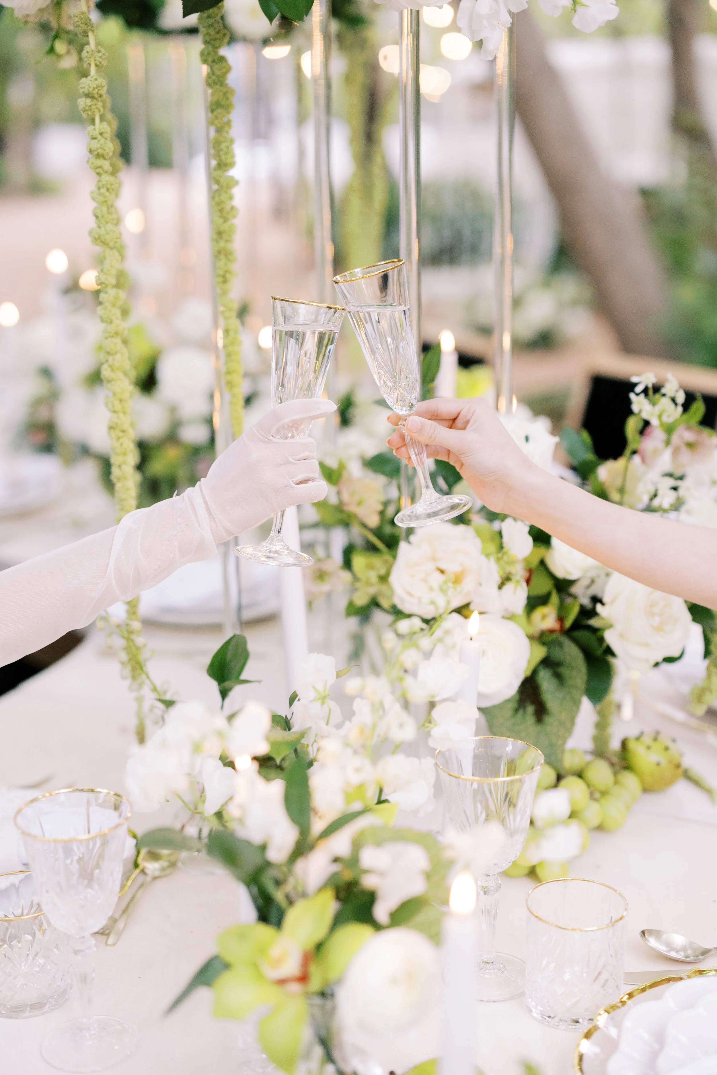 Two people clinking champagne glasses at a wedding reception table decorated with white flowers and candles.