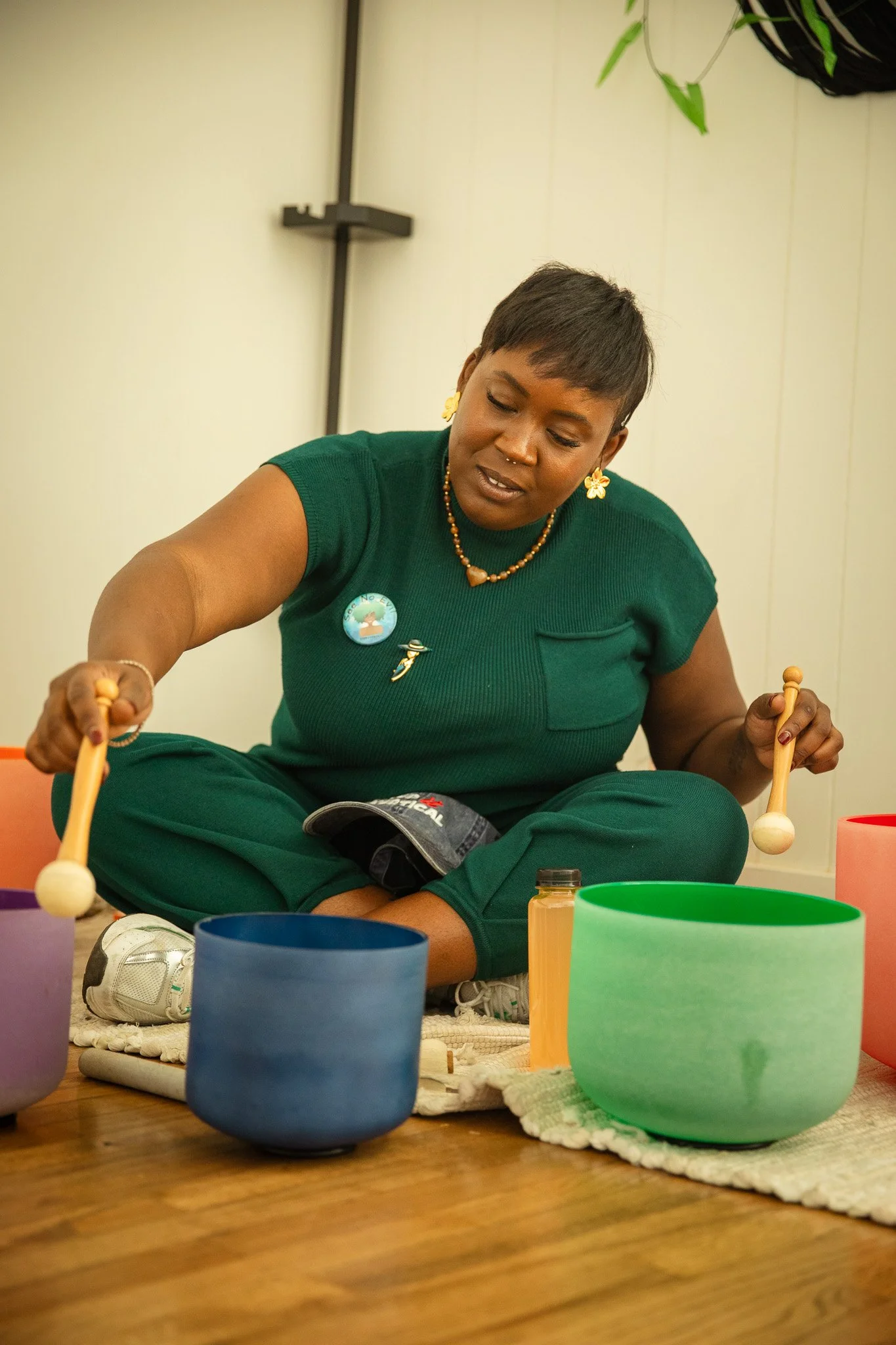 A woman sitting cross-legged on the floor, playing a set of colorful musical bowls with wooden mallets.