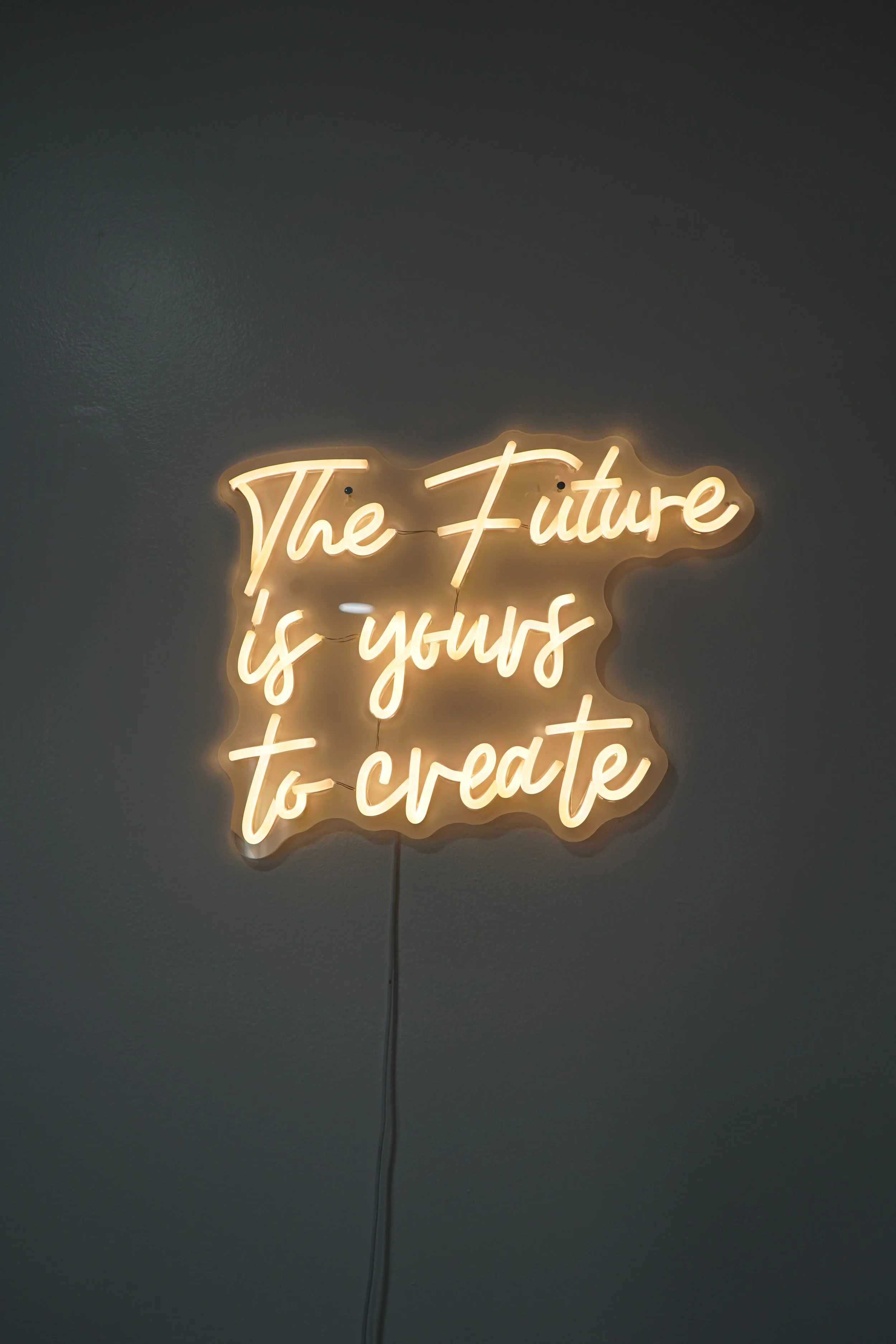 Neon sign with the quote 'The Future is yours to create' on a plain wall.