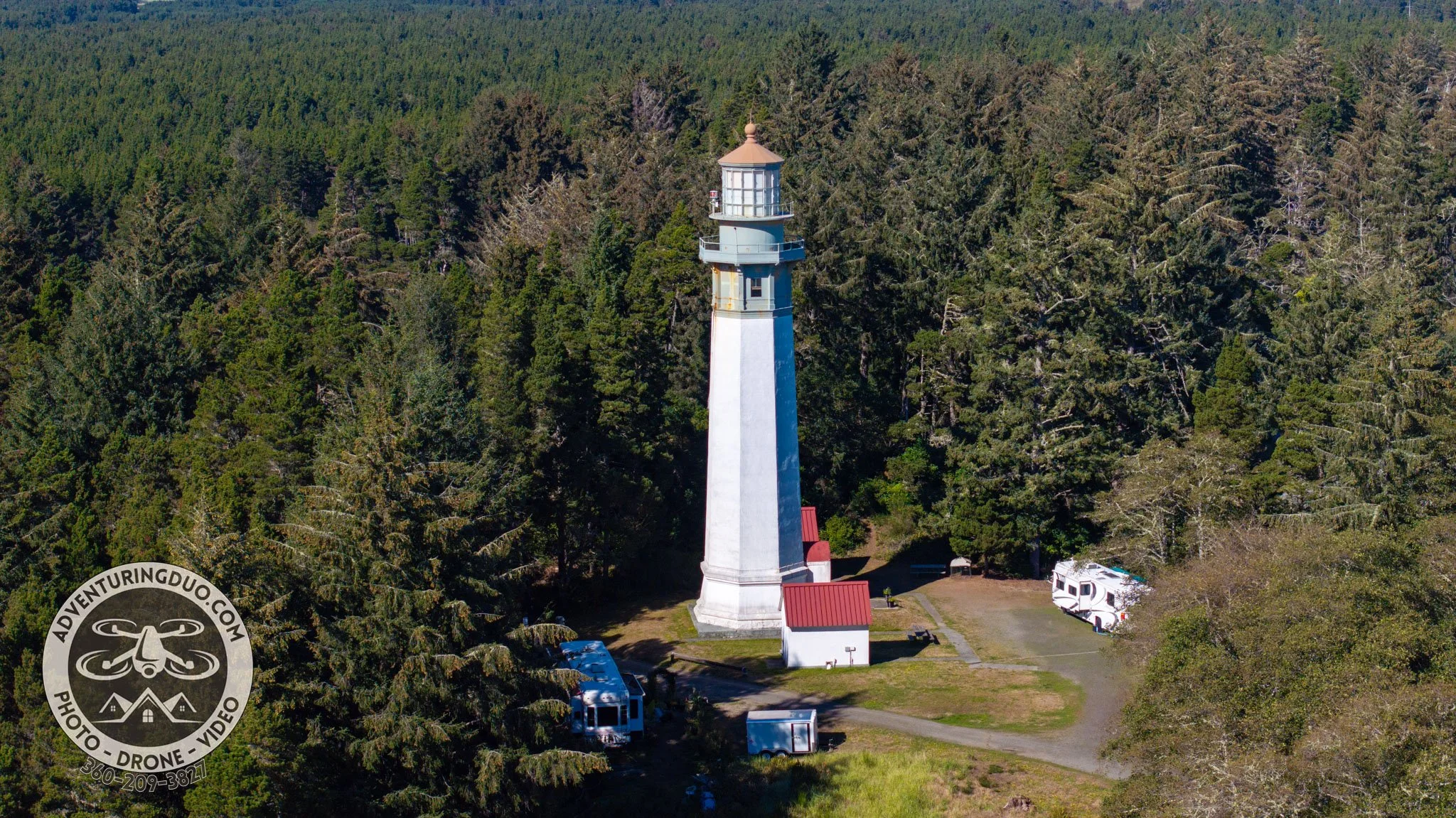  A stunning aerial drone photography capture of the Grays Harbor Lighthouse in Westport, Washington, surrounded by lush green forests with the Pacific Ocean and coastal town in the background.  AdventuringDuo.com   