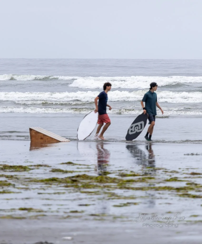 two male skimboard riders walking away from a rail jump dragging their boards. Grayland, Washington