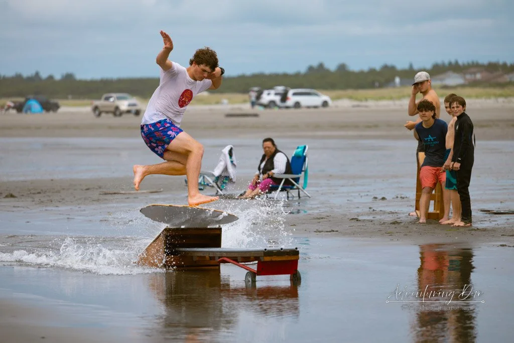 a group of skimboard riders watching one do a trick off a ramp. Grayland, Washington