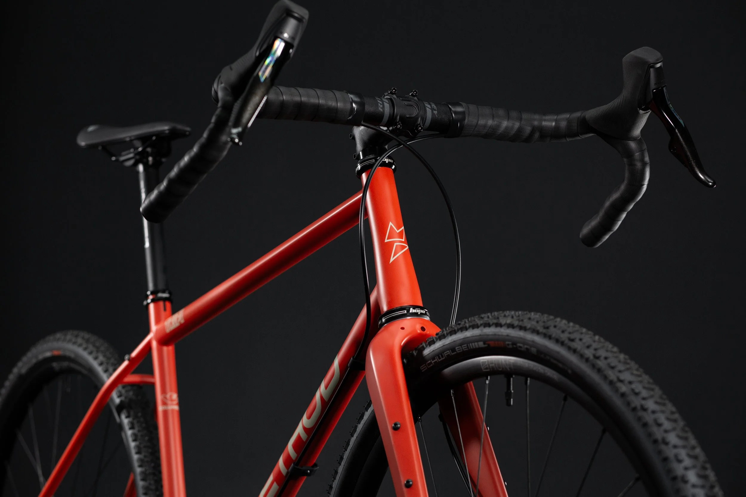 Close-up of the front of a red Method Frameworks Tripi gravel bike, showing the handlebars, logo, and Columbus carbon fork.