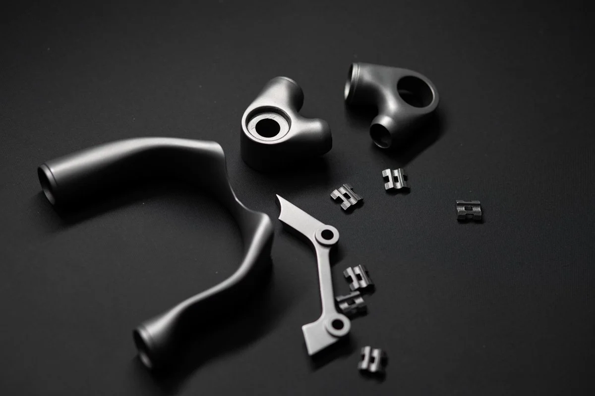 A selection of individual titanium 3D printed parts layed out on a table before they are assembled into on of the bicycle frames made in house.