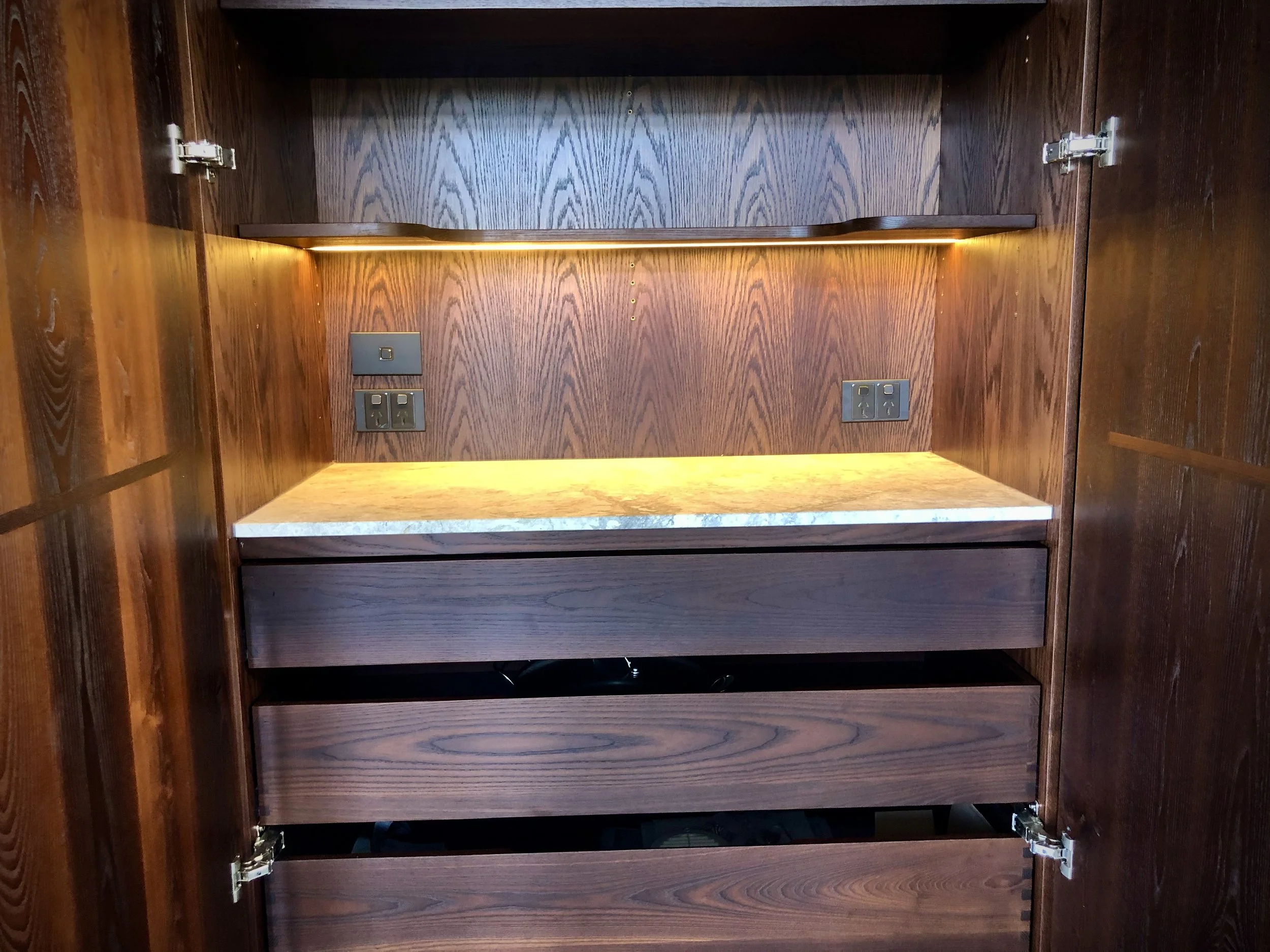 Empty wooden cabinet with built-in electrical outlets and LED lighting.