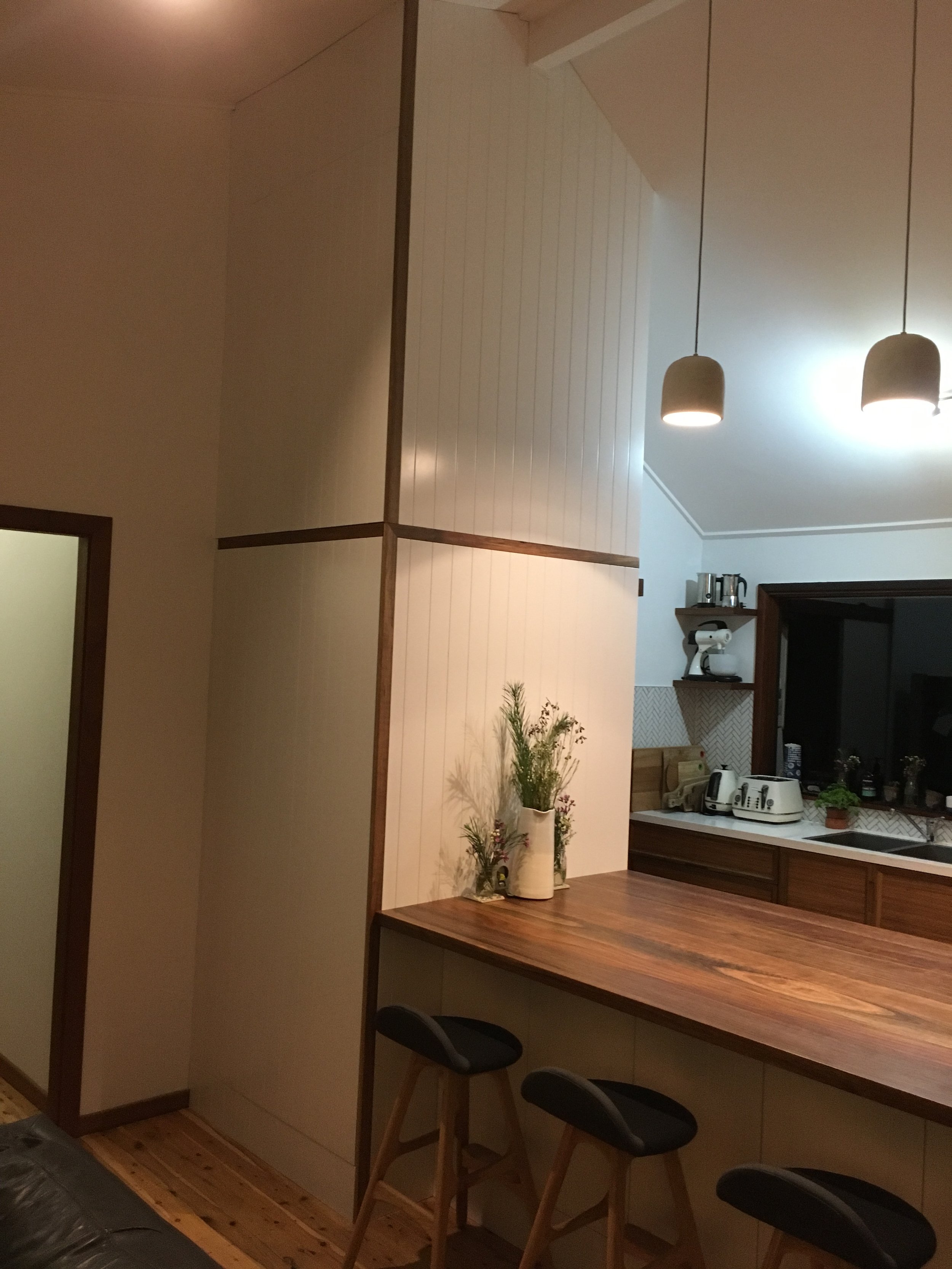 Kitchen with white walls, dark wood cabinets, a wooden countertop, and two roasting chairs at the counter. There are hanging pendant lights and kitchen appliances on a shelf.