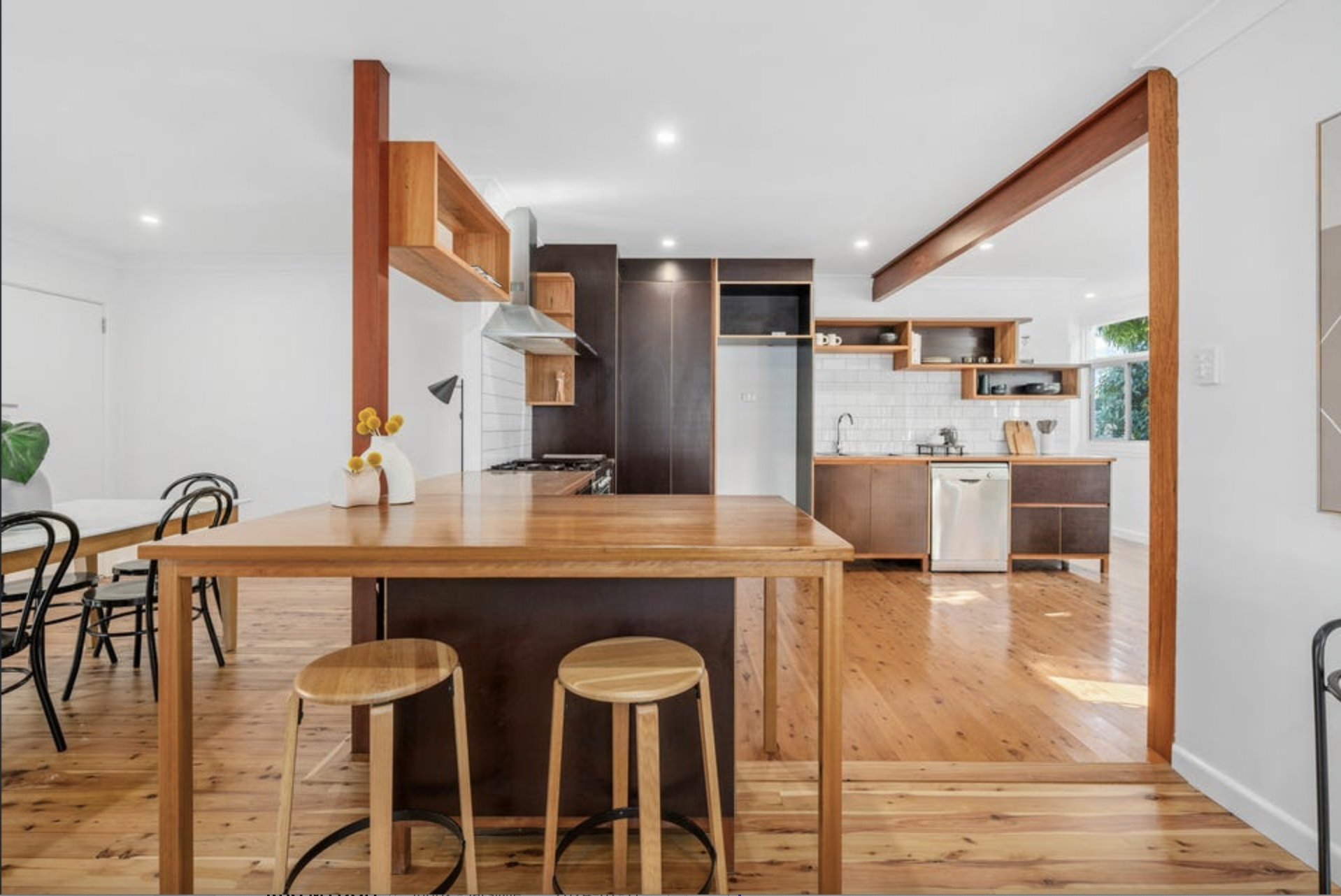 Open plan kitchen and dining area with wooden floors, white walls, and wooden shelving and furniture.