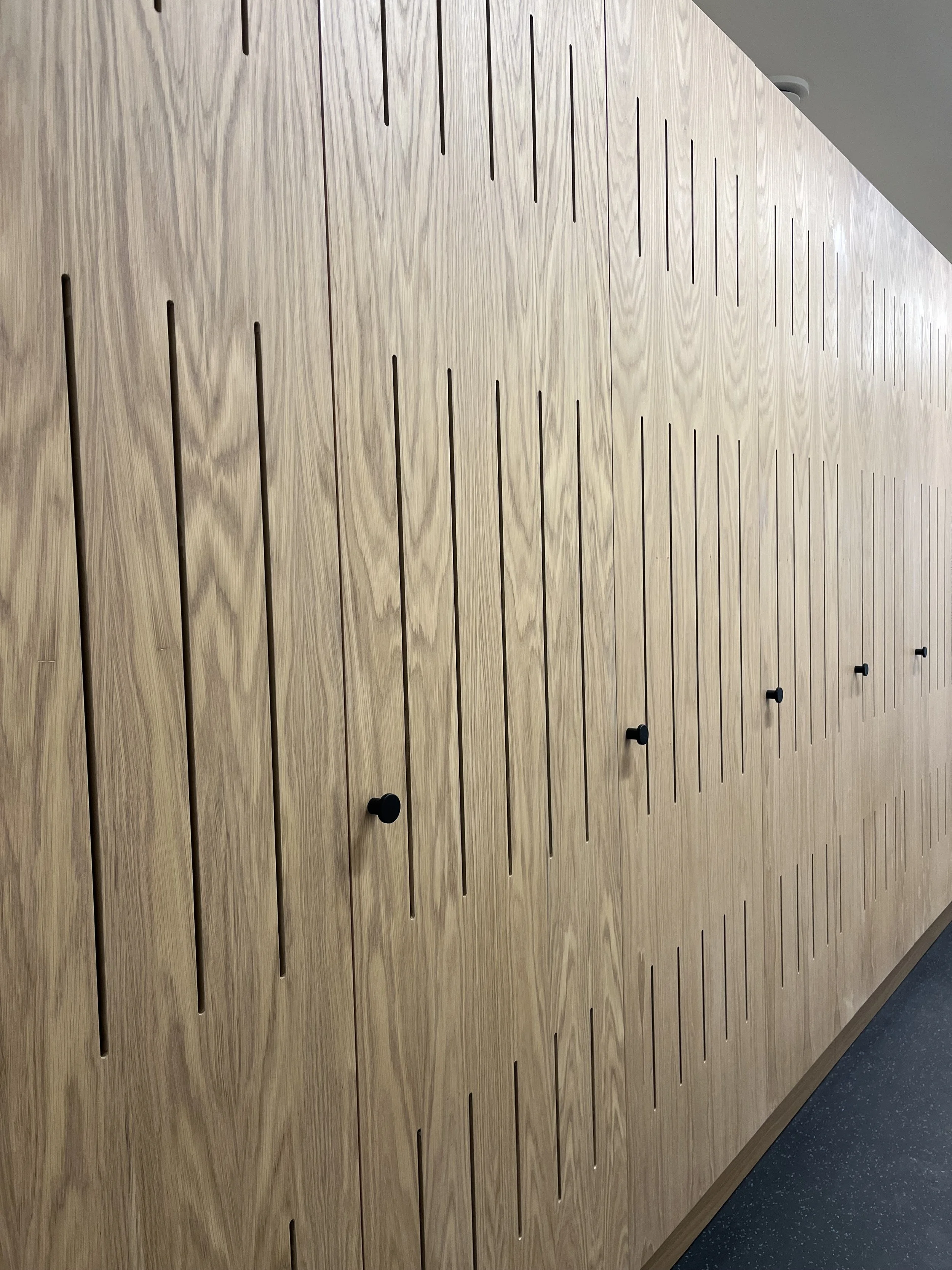Wooden wall with vertical slats and black knobs.