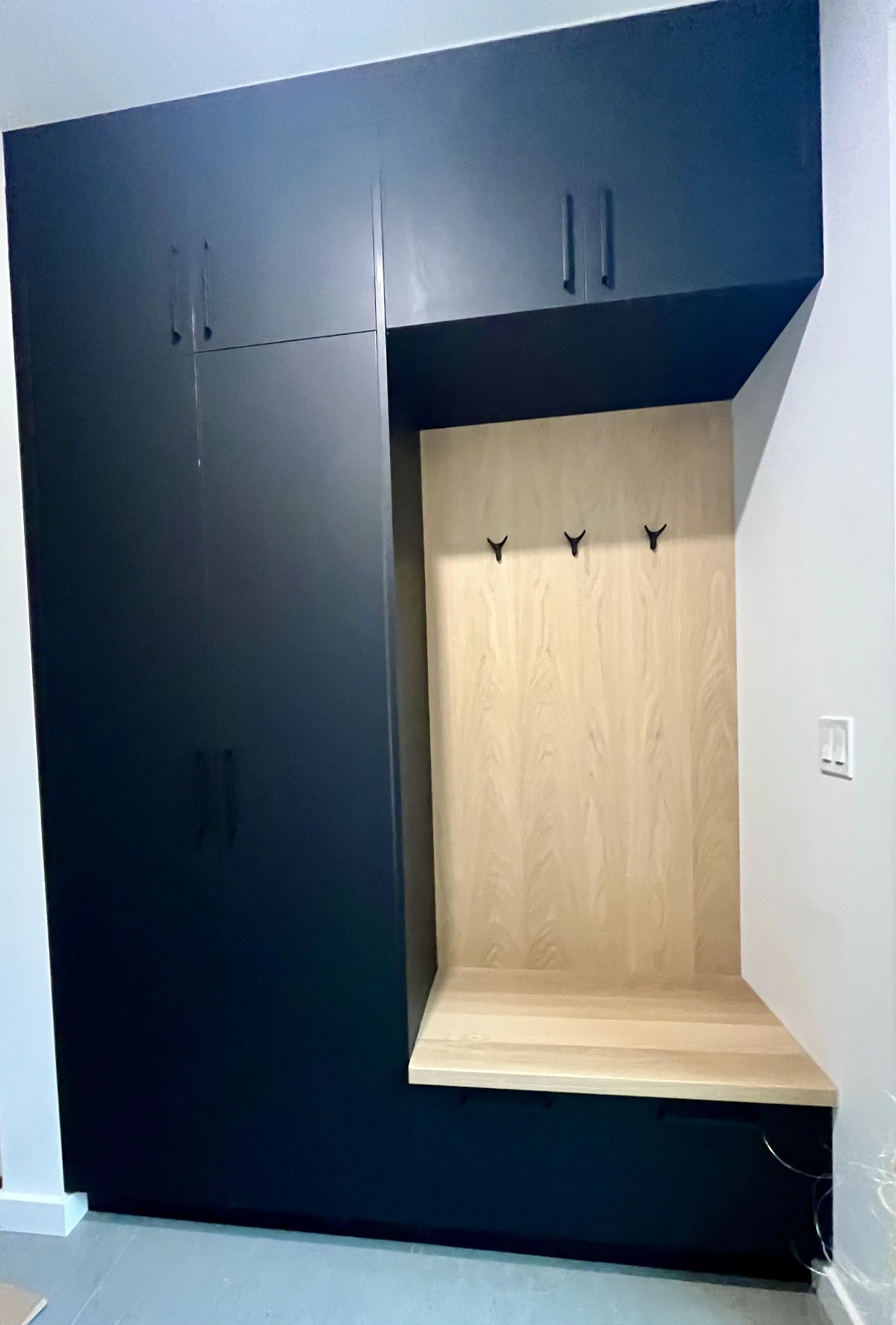 Modern black and wood entryway storage unit with hooks and cabinets.