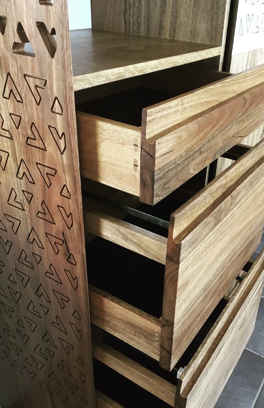 Close-up of wooden drawers with black inner sides, one drawer partially open, next to a wooden panel with geometric cutouts.