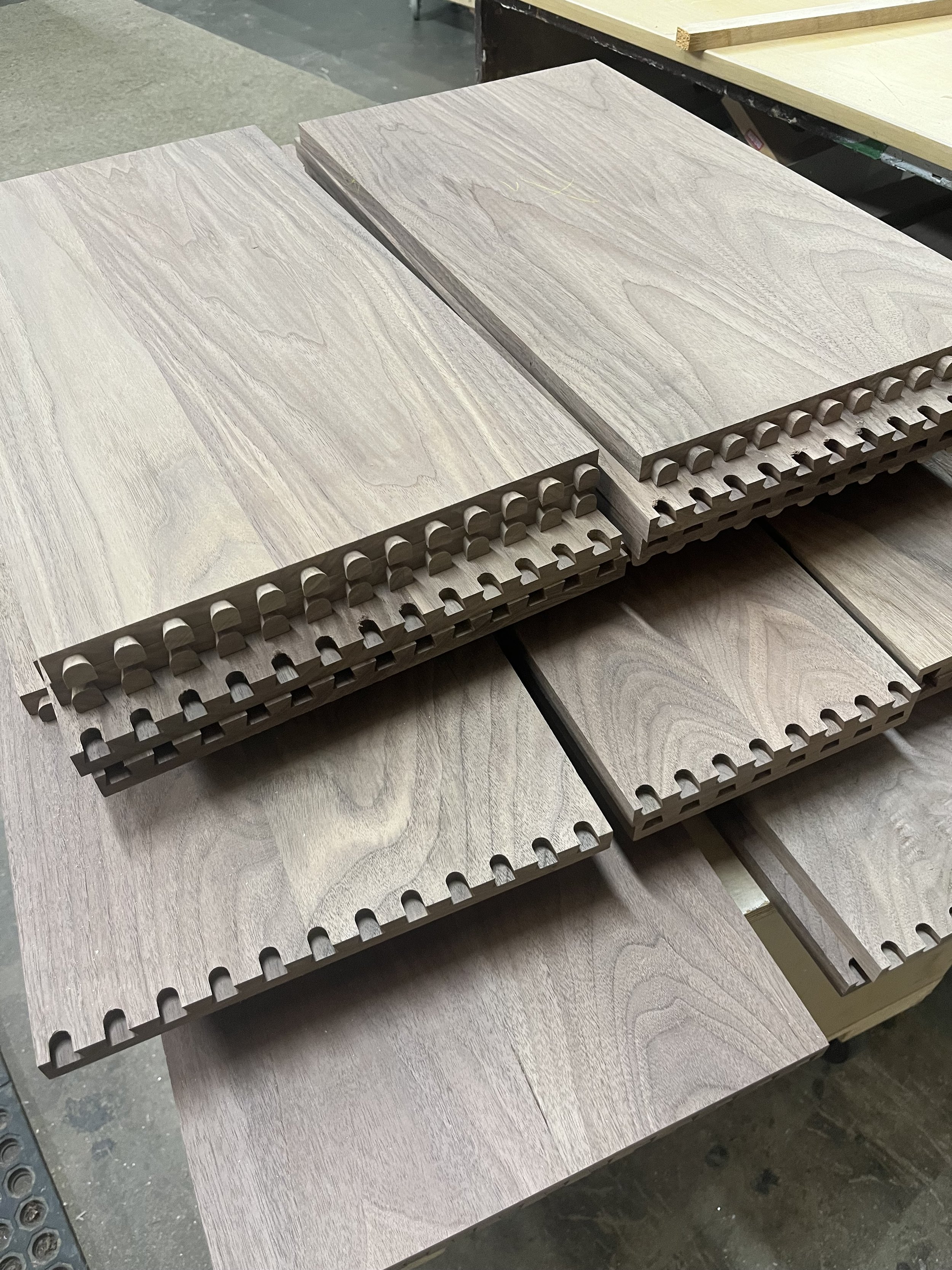 Stacks of unfinished wooden flooring planks with tongue and groove edges, in a woodworking shop.