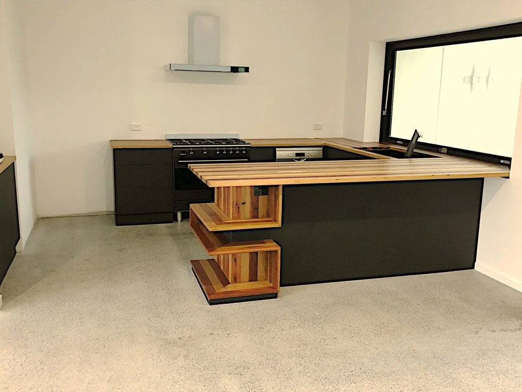 Modern kitchen with black cabinets, wooden countertop, and open shelving, located near a large window.