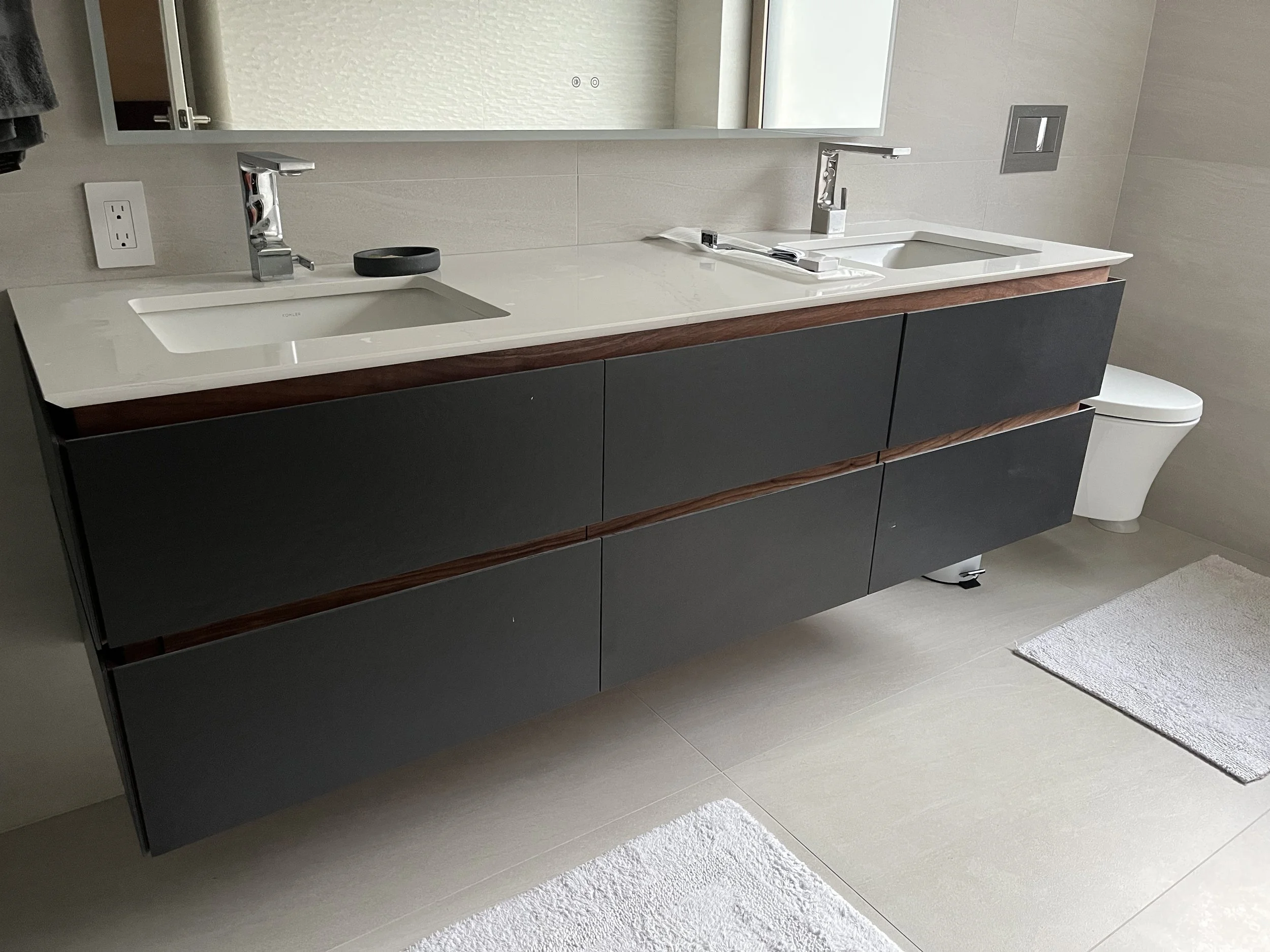 Modern bathroom with dual sinks, black vanity, large mirror, and a toilet in the background.