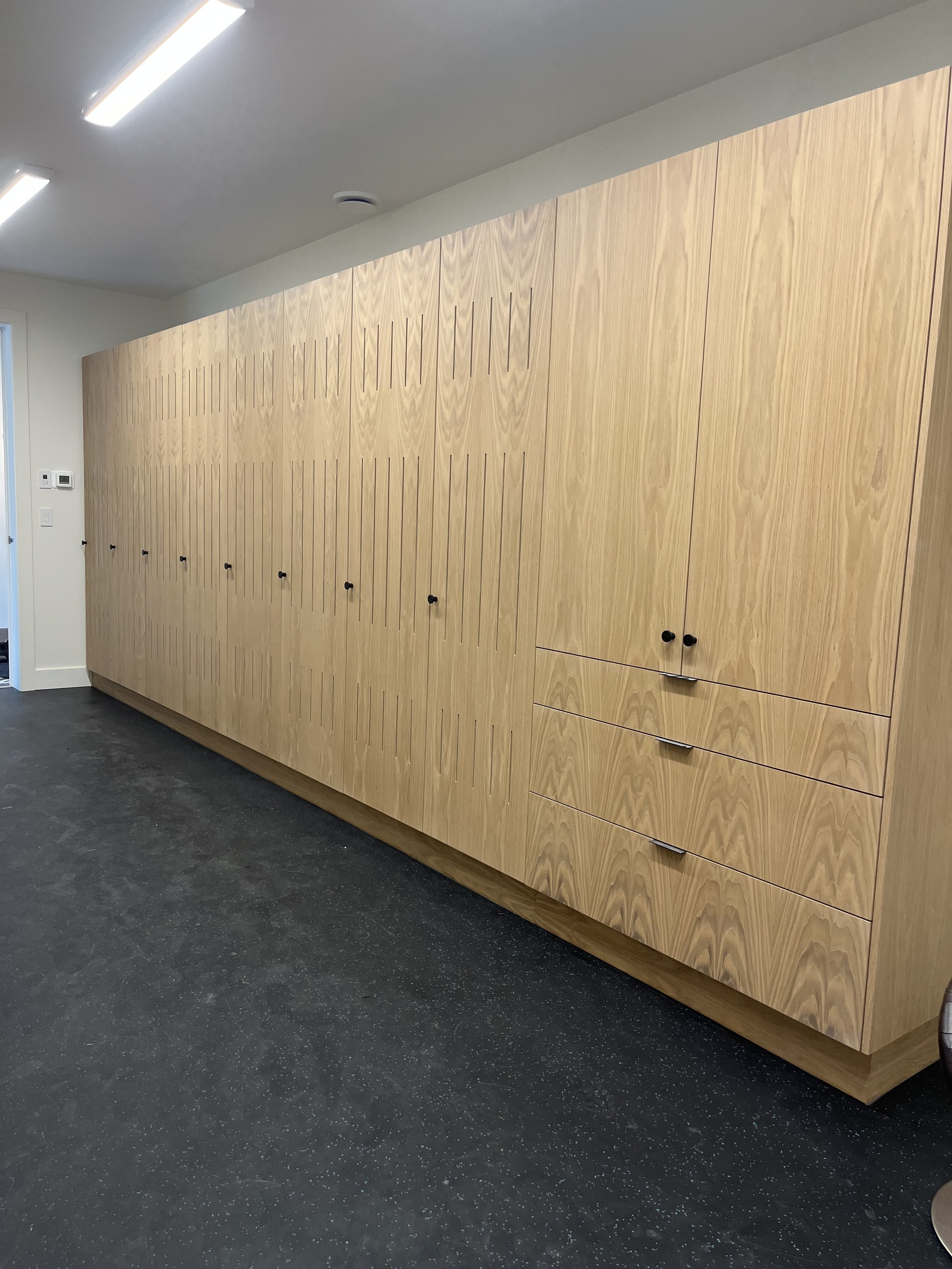 A long wooden locker with black handles, built into a wall in a modern interior space.