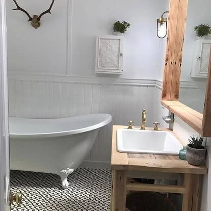 Bathroom with a clawfoot bathtub, a wooden vanity with a white sink, a mirror, a small potted plant, and decorative wall accents.