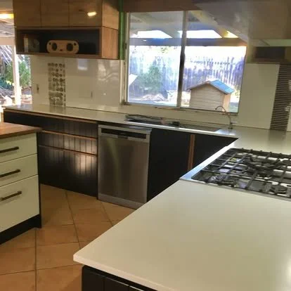 Kitchen with white countertops, black lower cabinets, stove, dishwasher, and a window showing an outdoor area with a dog house.