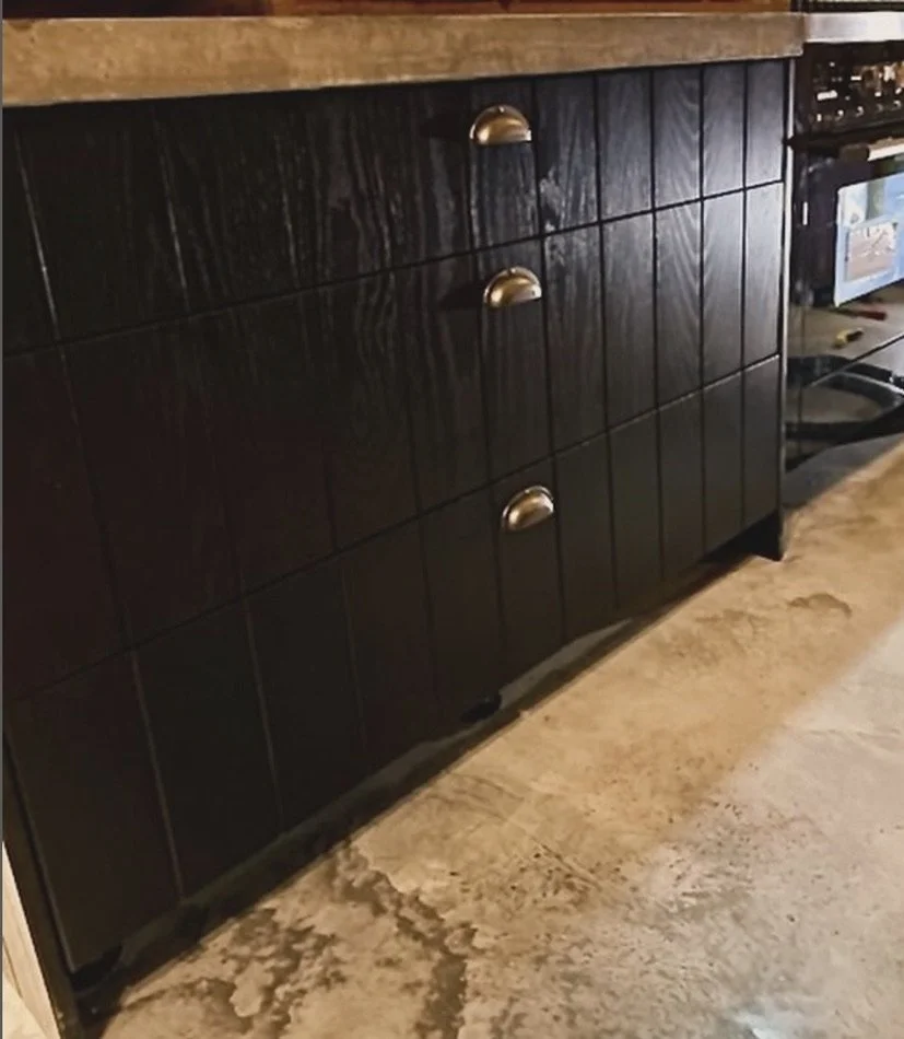 Close-up of a wooden kitchen cabinet with metallic handles, set on a concrete floor next to a stove.