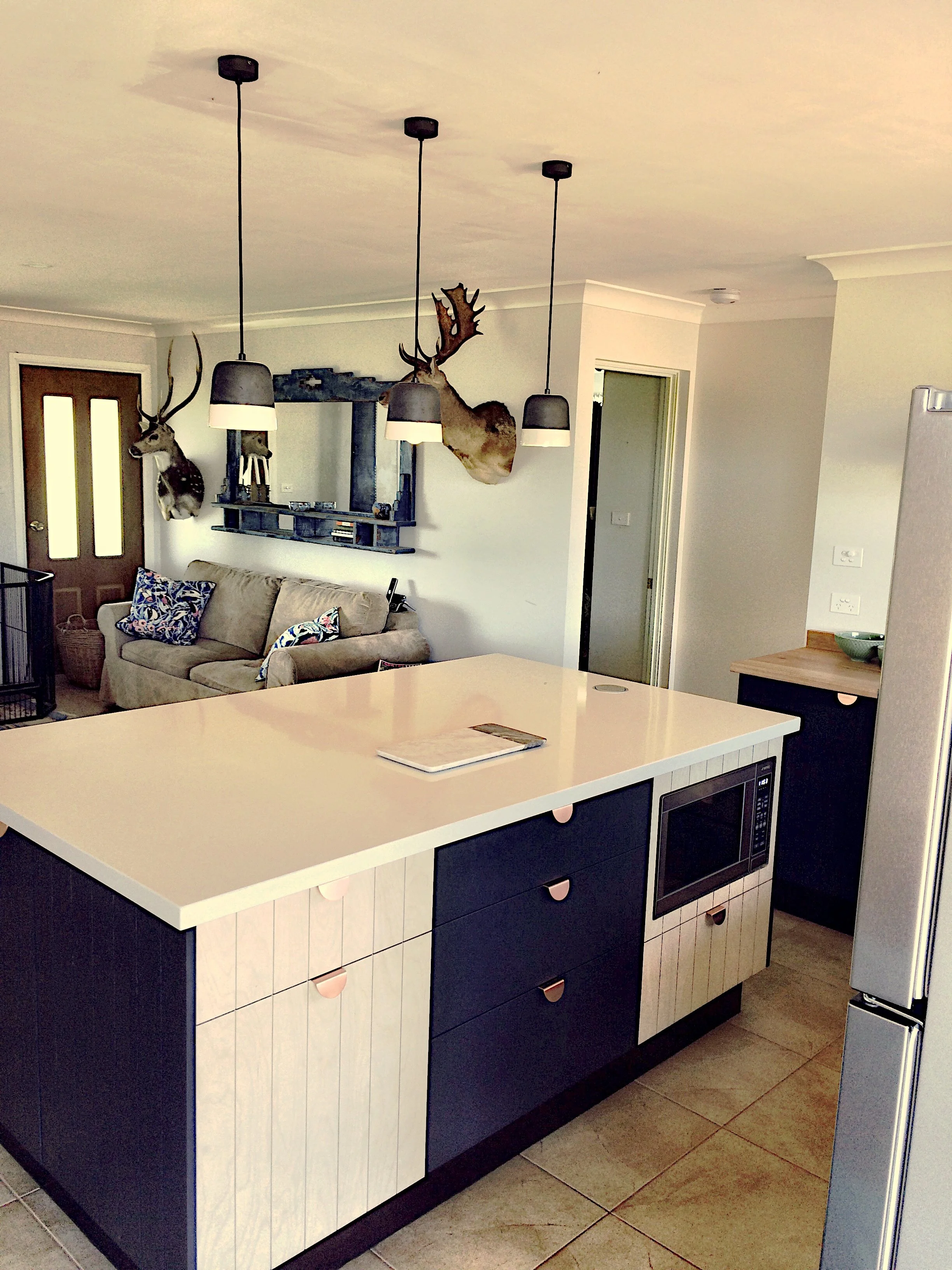 Open kitchen with a large island, black and white cabinetry, a microwave, and a living room with a sofa and mounted deer and elk heads.