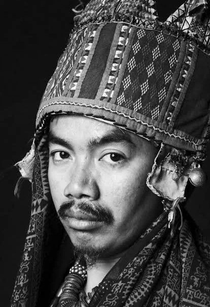 Portrait of a man wearing a traditional, patterned headscarf with decorative elements, looking directly at the camera.