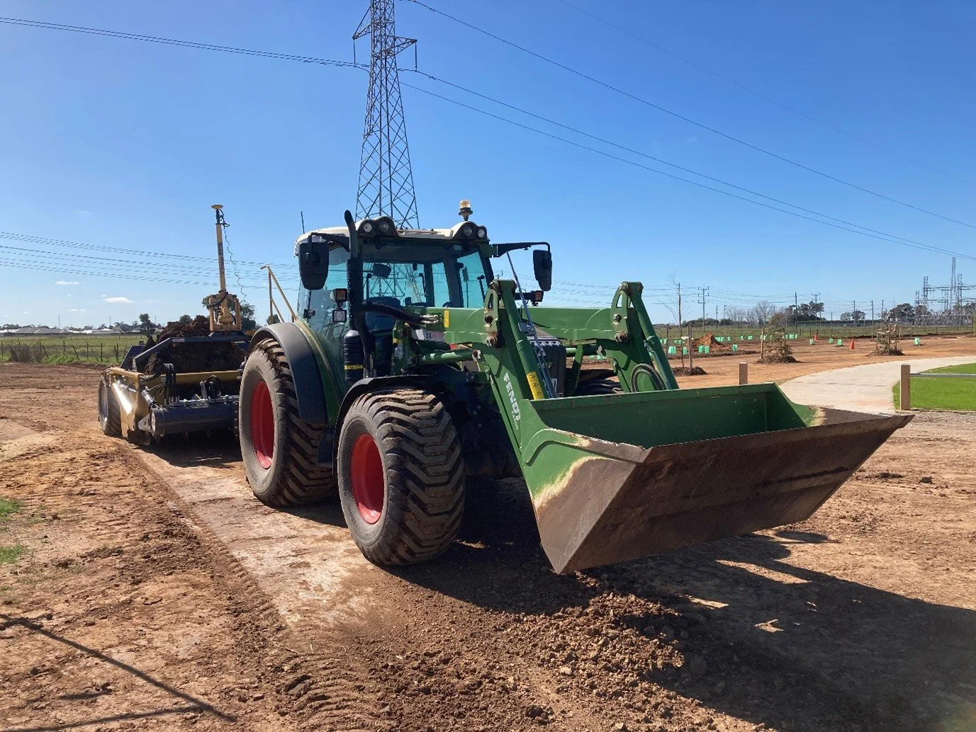 A green front loader tractor on a construction site with a clear blue sky overhead.