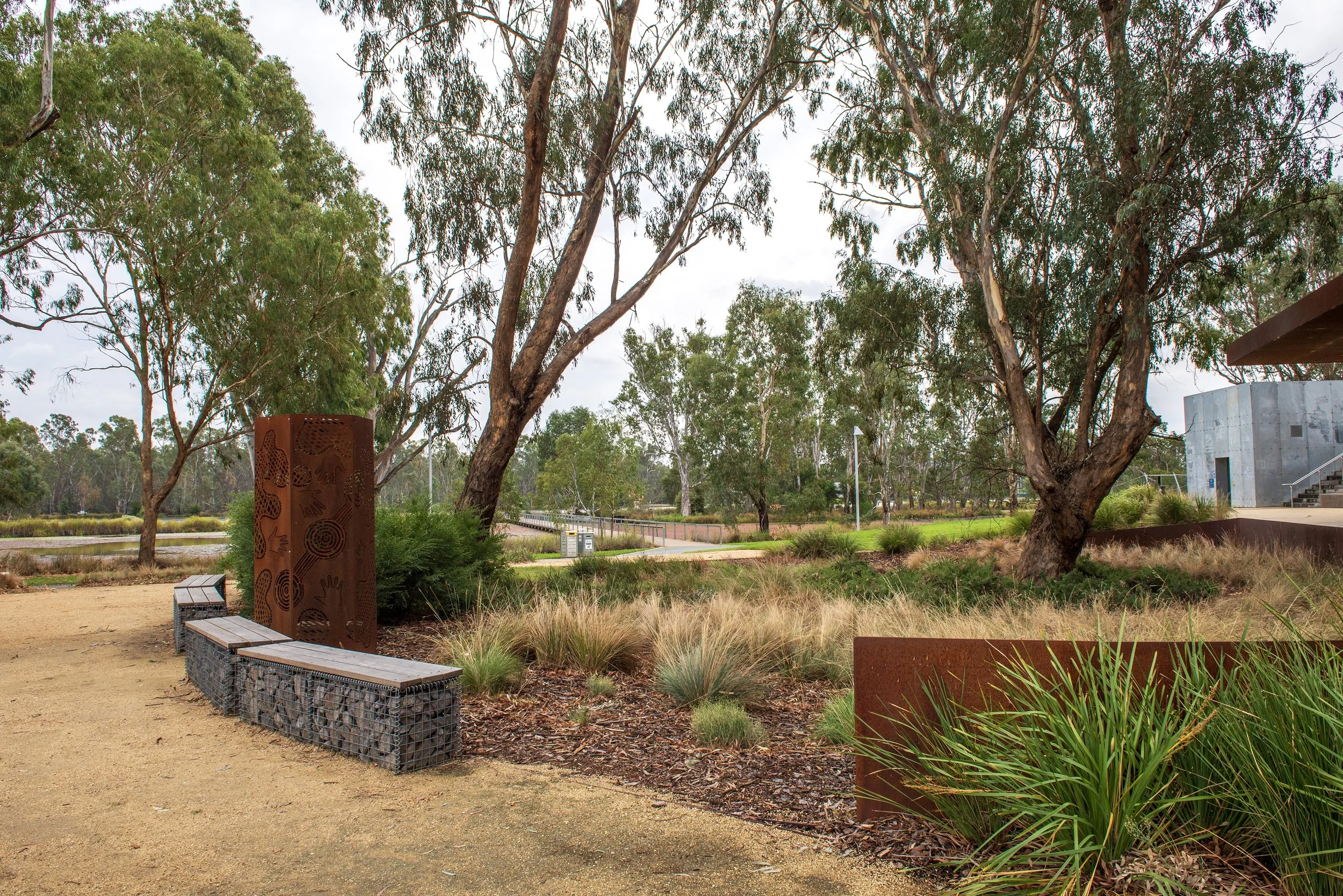 A peaceful park scene with trees, bushes, a bench, and a pathway on a cloudy day.