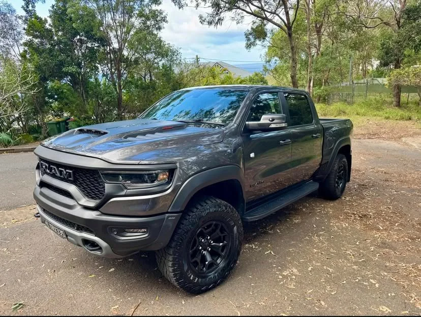 A gray RAM pickup truck parked on a gravel area surrounded by trees and greenery.