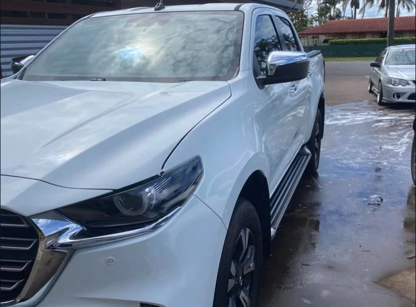 White pickup truck parked on a wet surface, with cars and trees in the background.